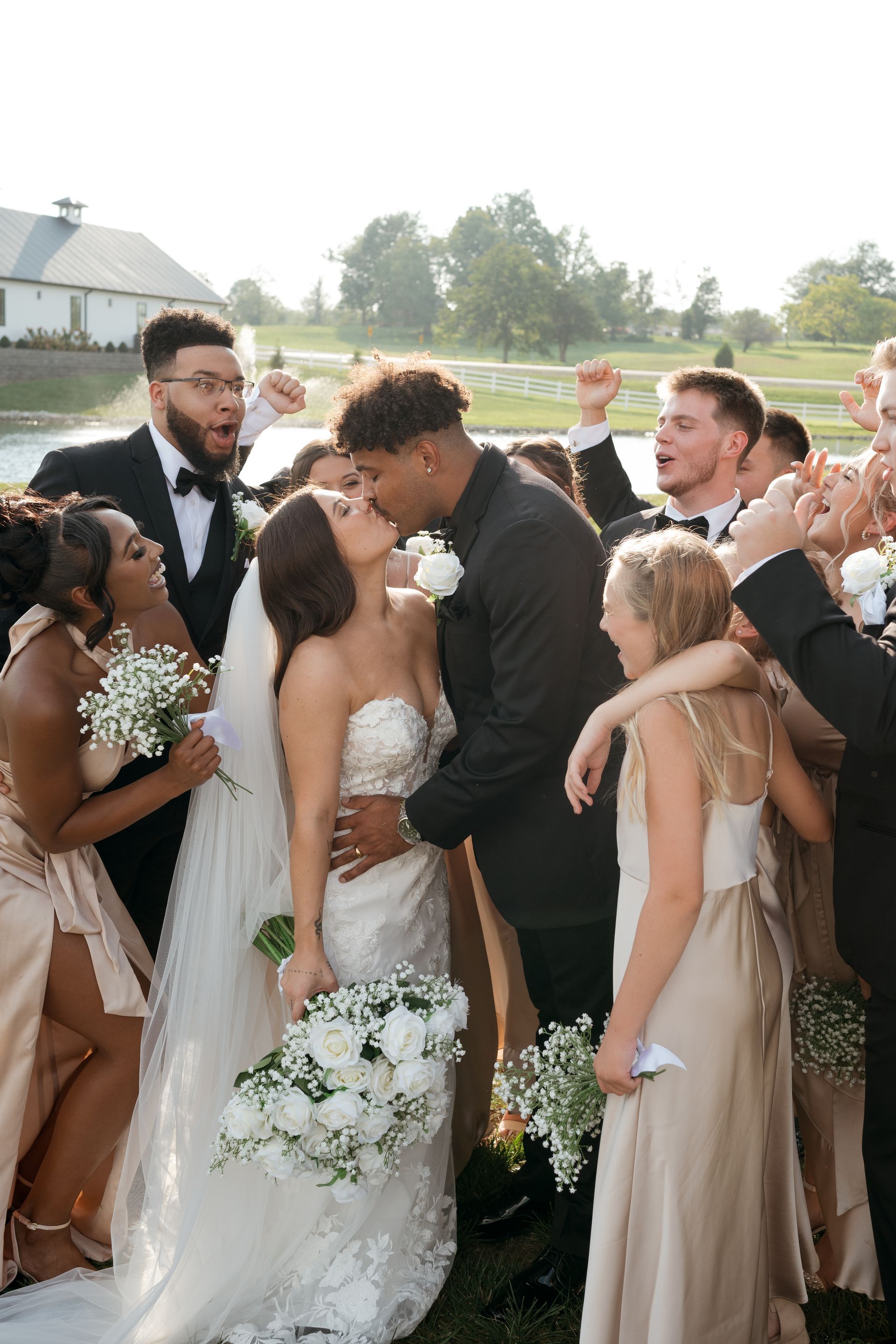 A bride and groom are kissing in front of their wedding party.