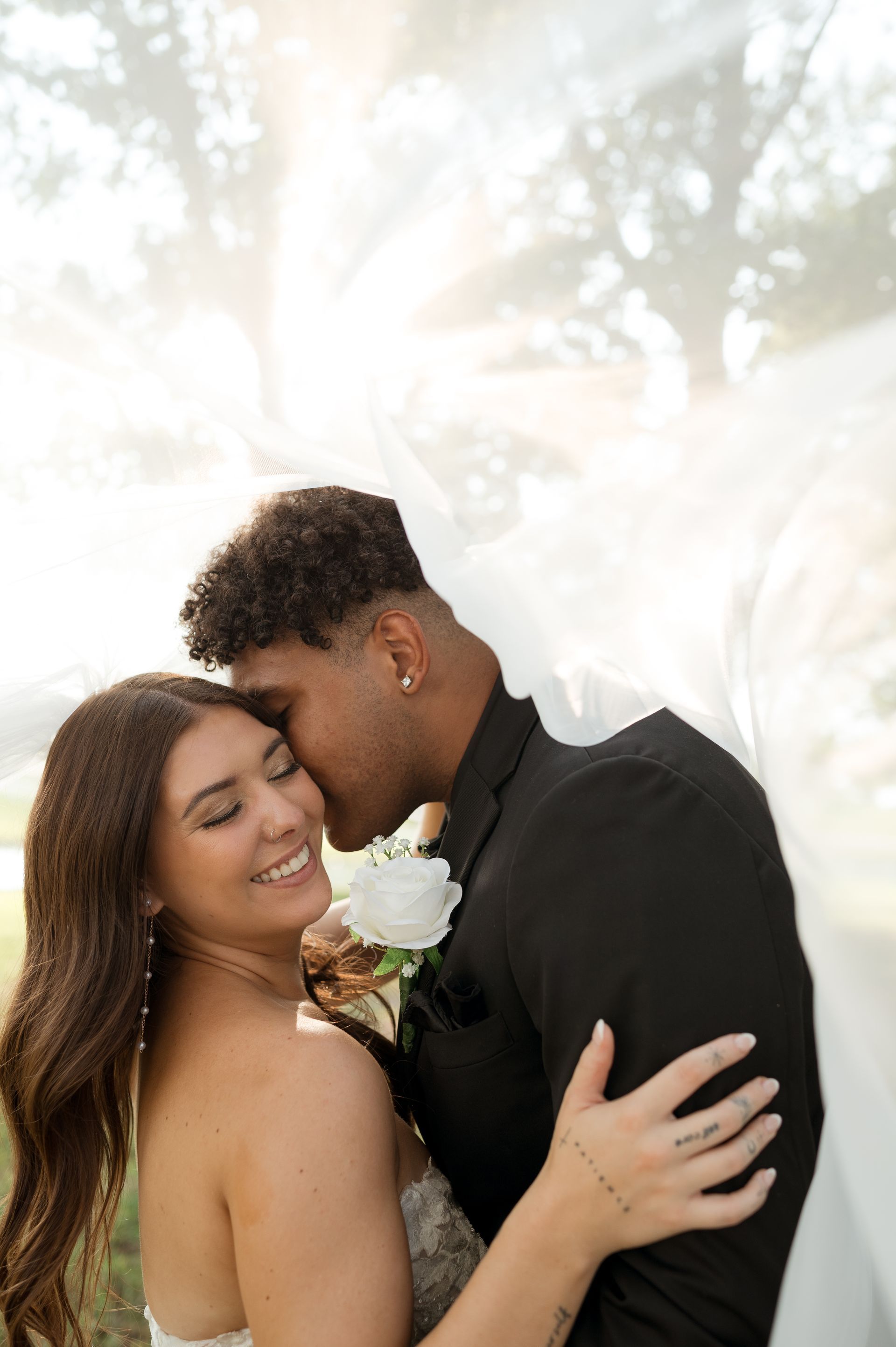 A bride and groom are kissing under a veil.