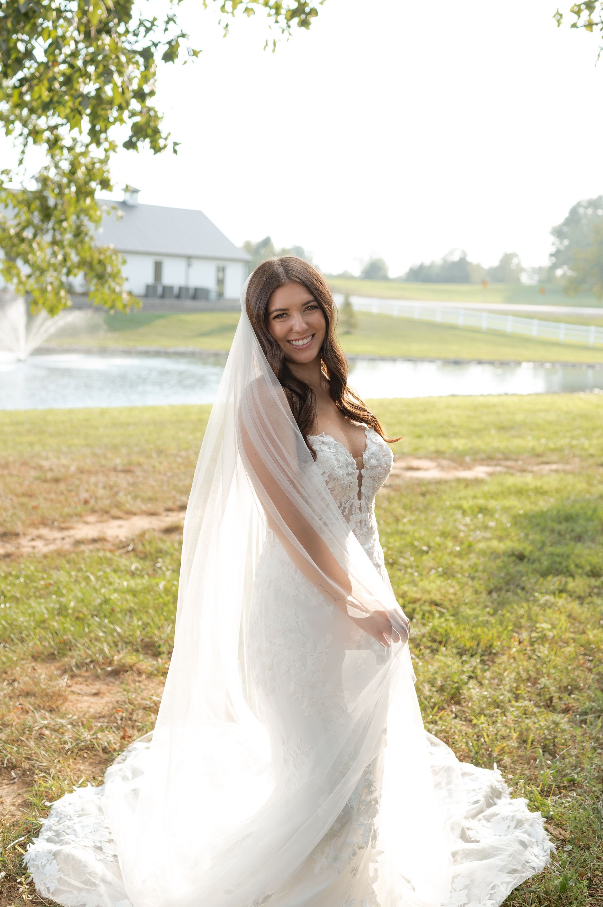 A bride in a wedding dress and veil is standing in a field.