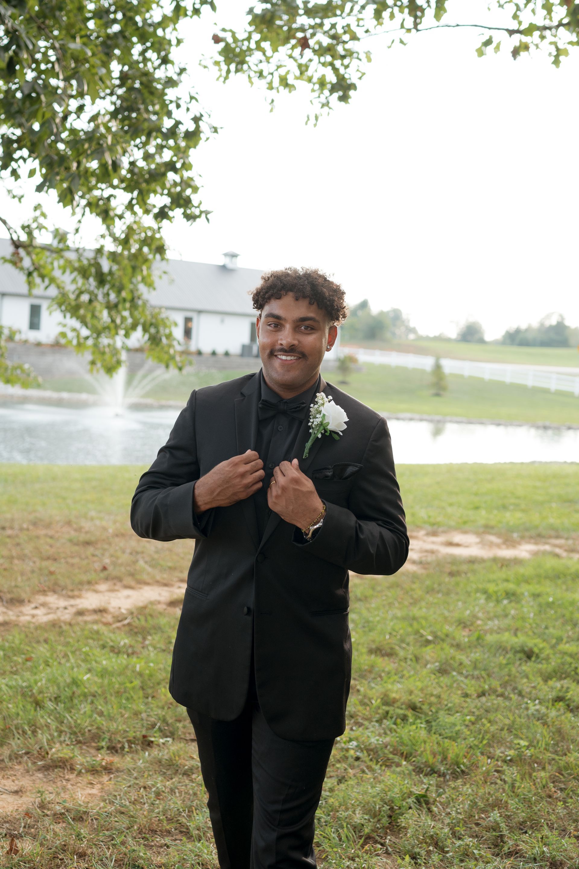 A man in a black suit and bow tie is standing in a field.