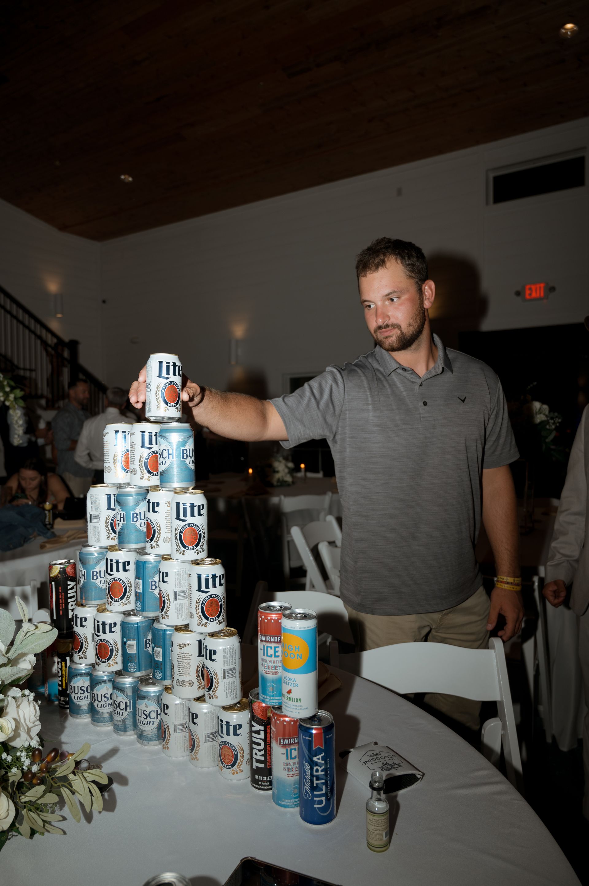 A man is stacking cans of beer on top of each other on a table.