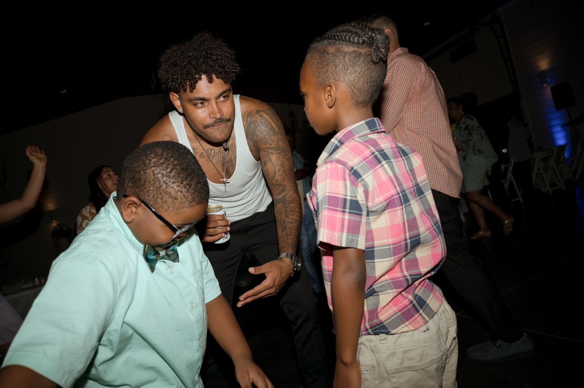 A man in a white tank top is talking to two young boys at a party.