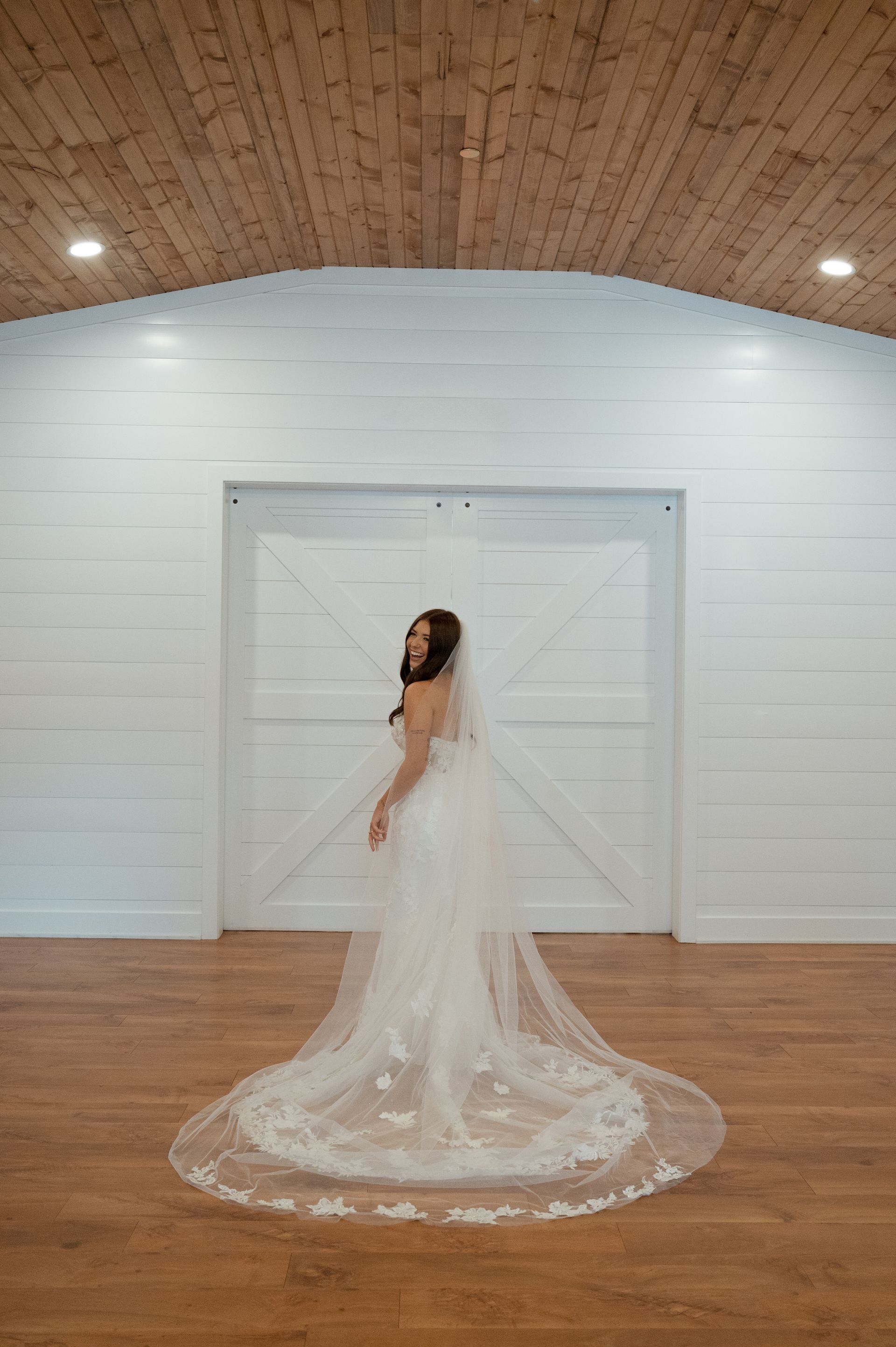 A bride in a wedding dress and veil is standing in front of a white barn door.