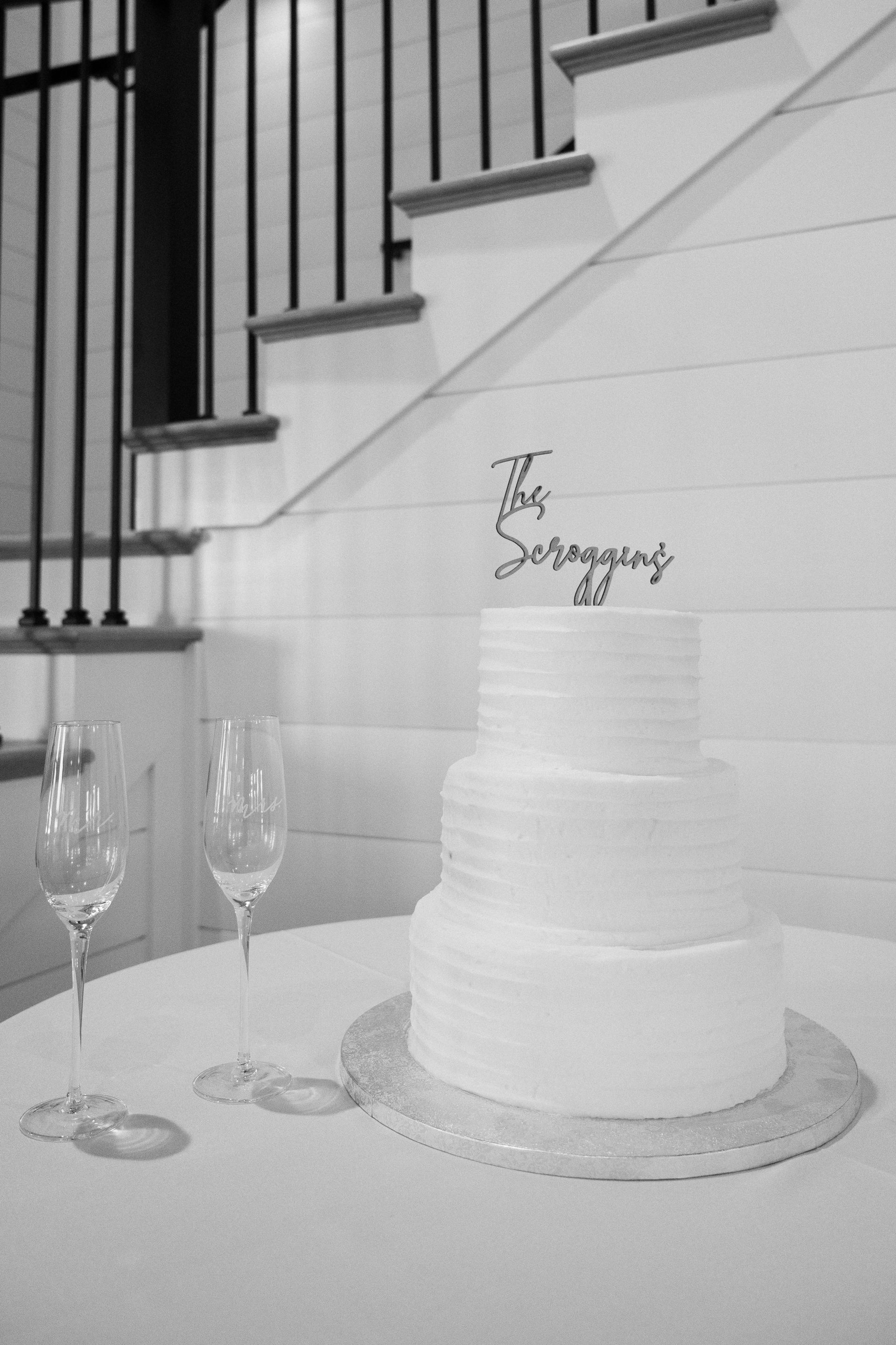 A black and white photo of a wedding cake and wine glasses on a table.