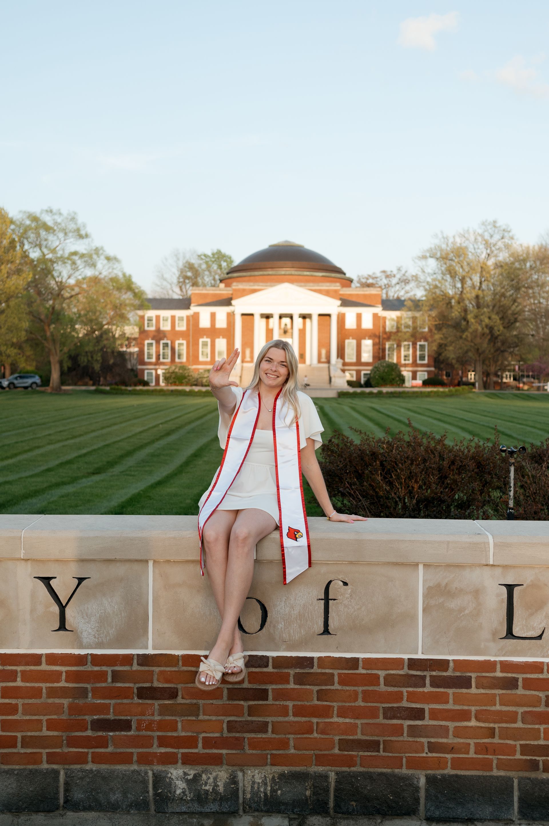 A woman is sitting on a brick wall in front of a building.