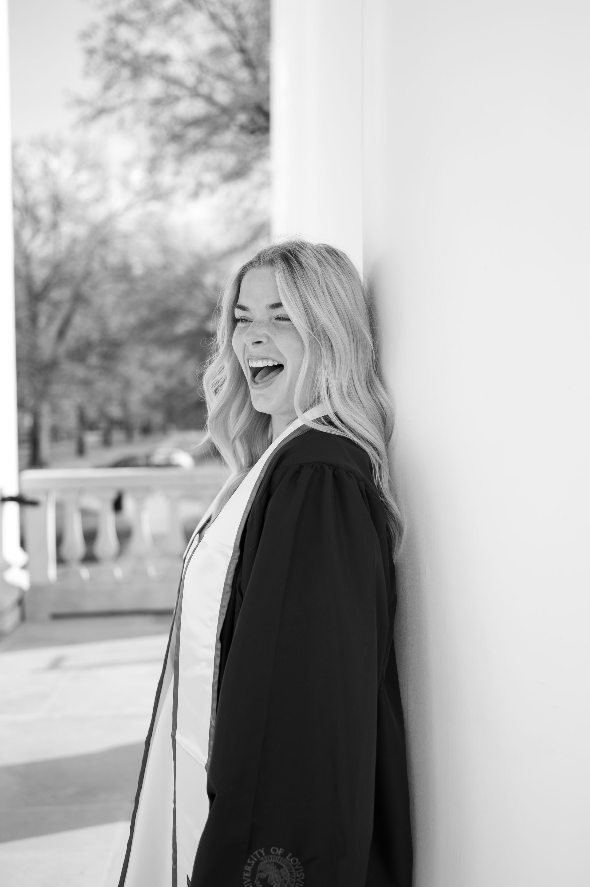 A black and white photo of a woman in a graduation cap and gown laughing.
