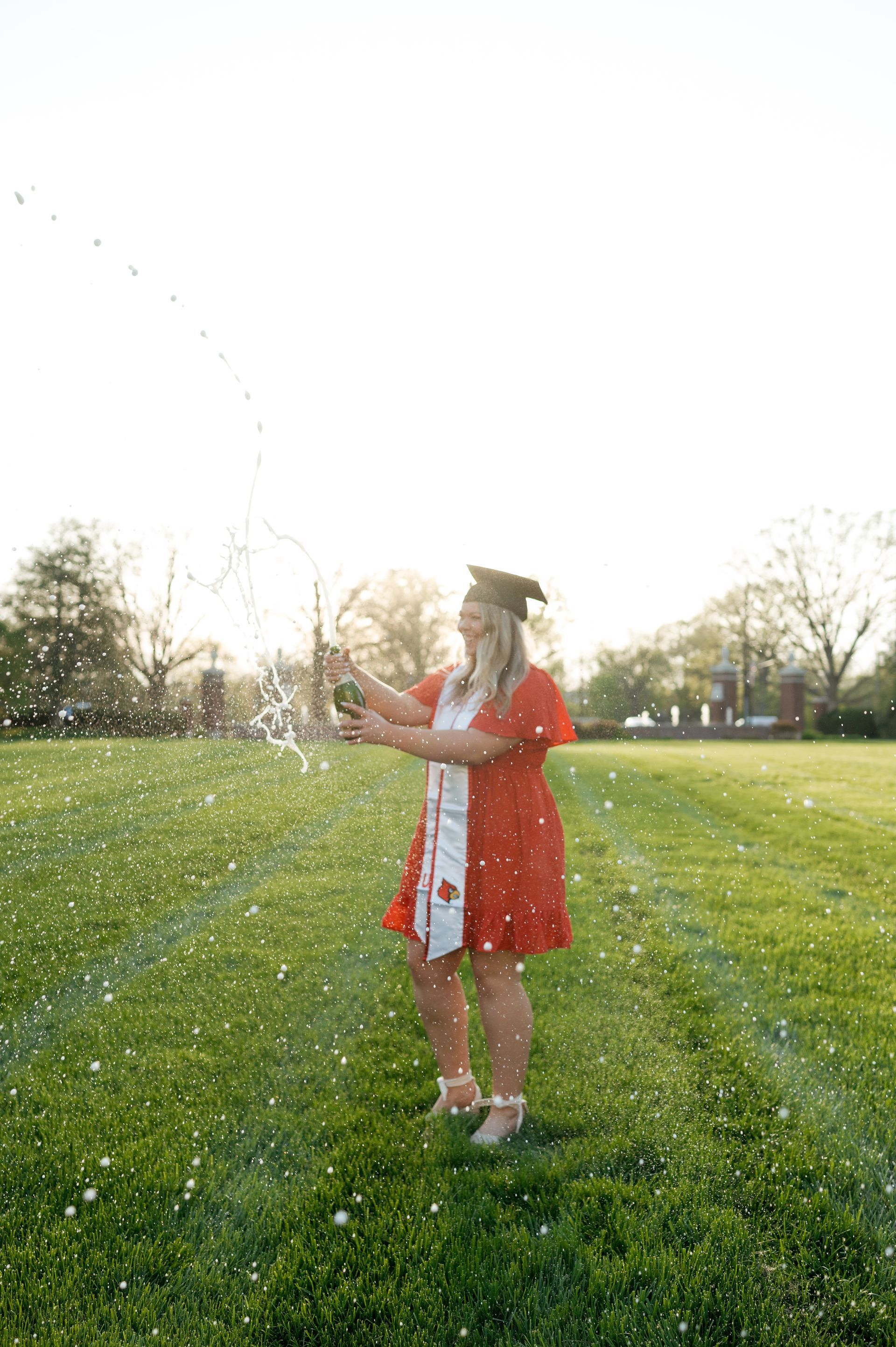 A woman in a graduation cap and gown is throwing confetti in a field.
