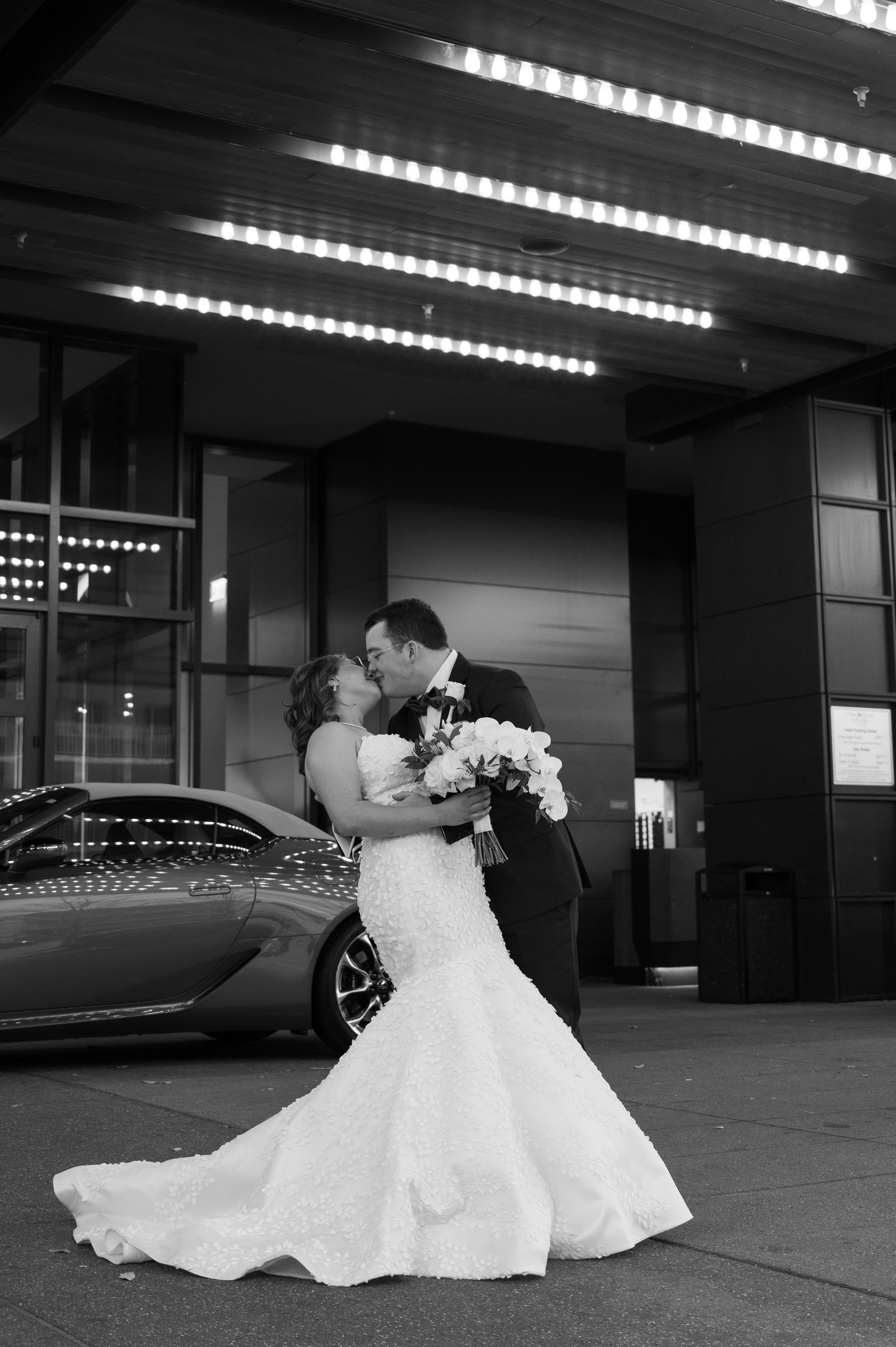 A bride and groom kissing in front of a car