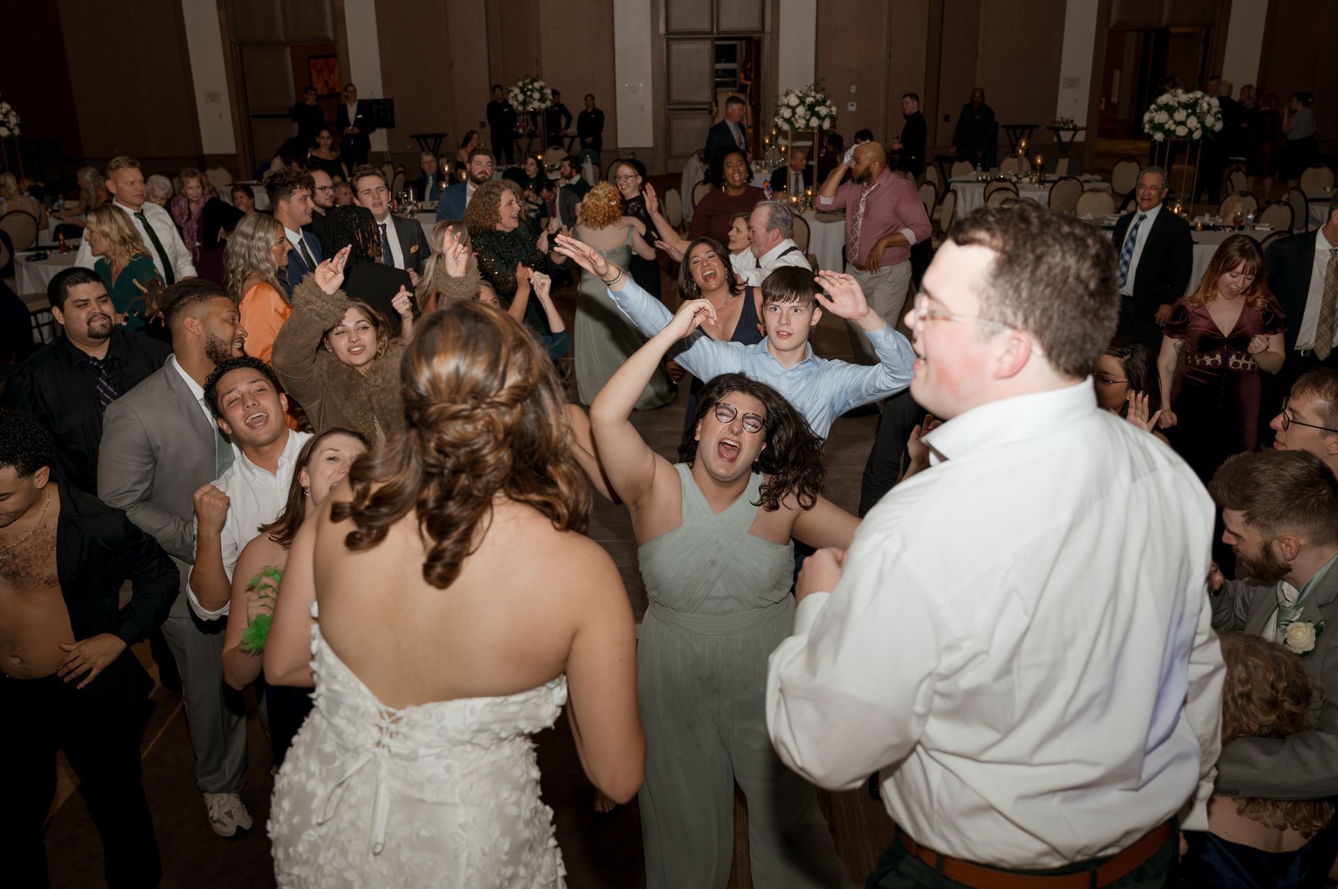 A bride and groom are dancing with their wedding guests at a wedding reception.
