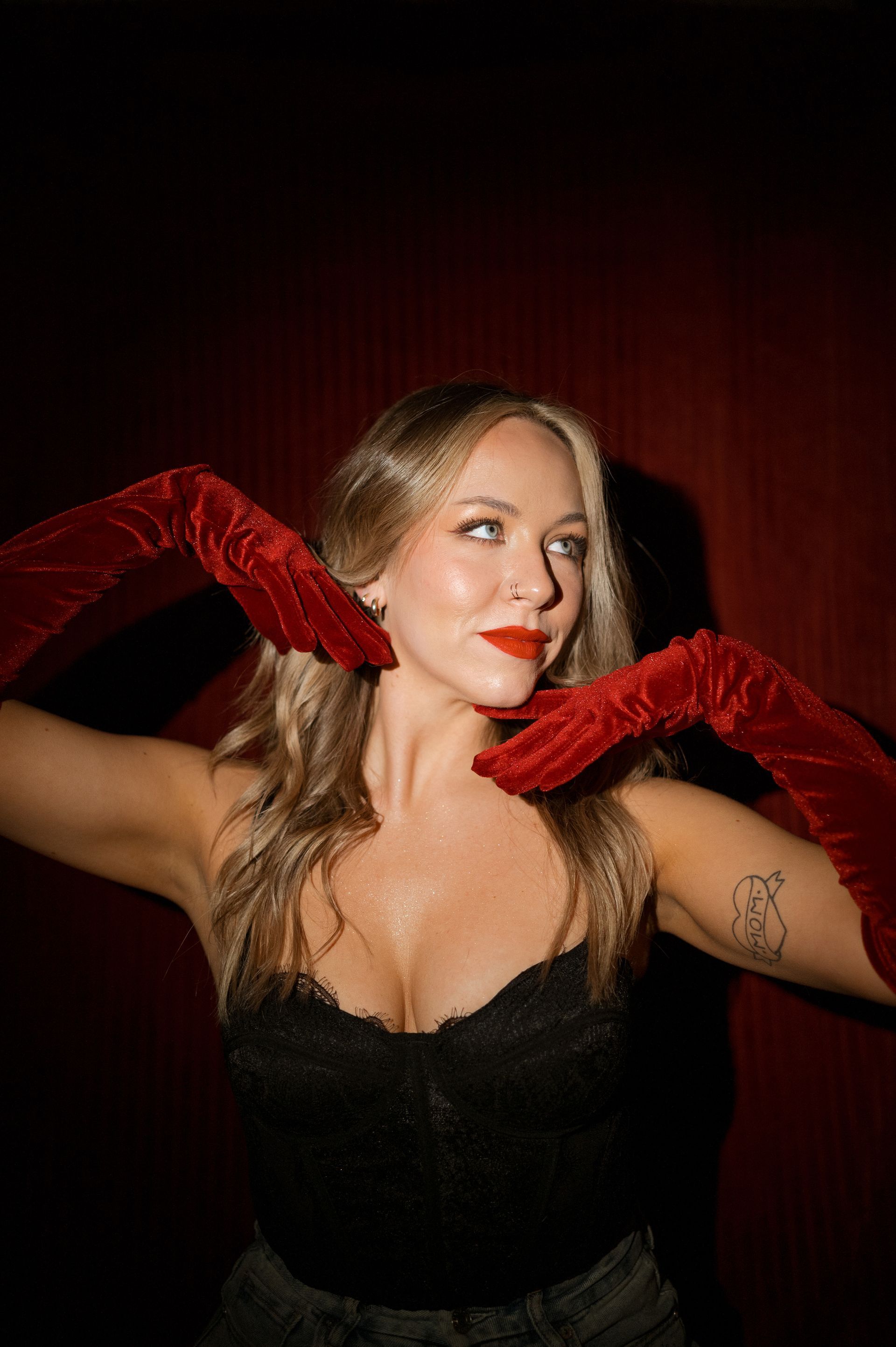 A woman in a black top and red gloves is making a heart shape with her hands.