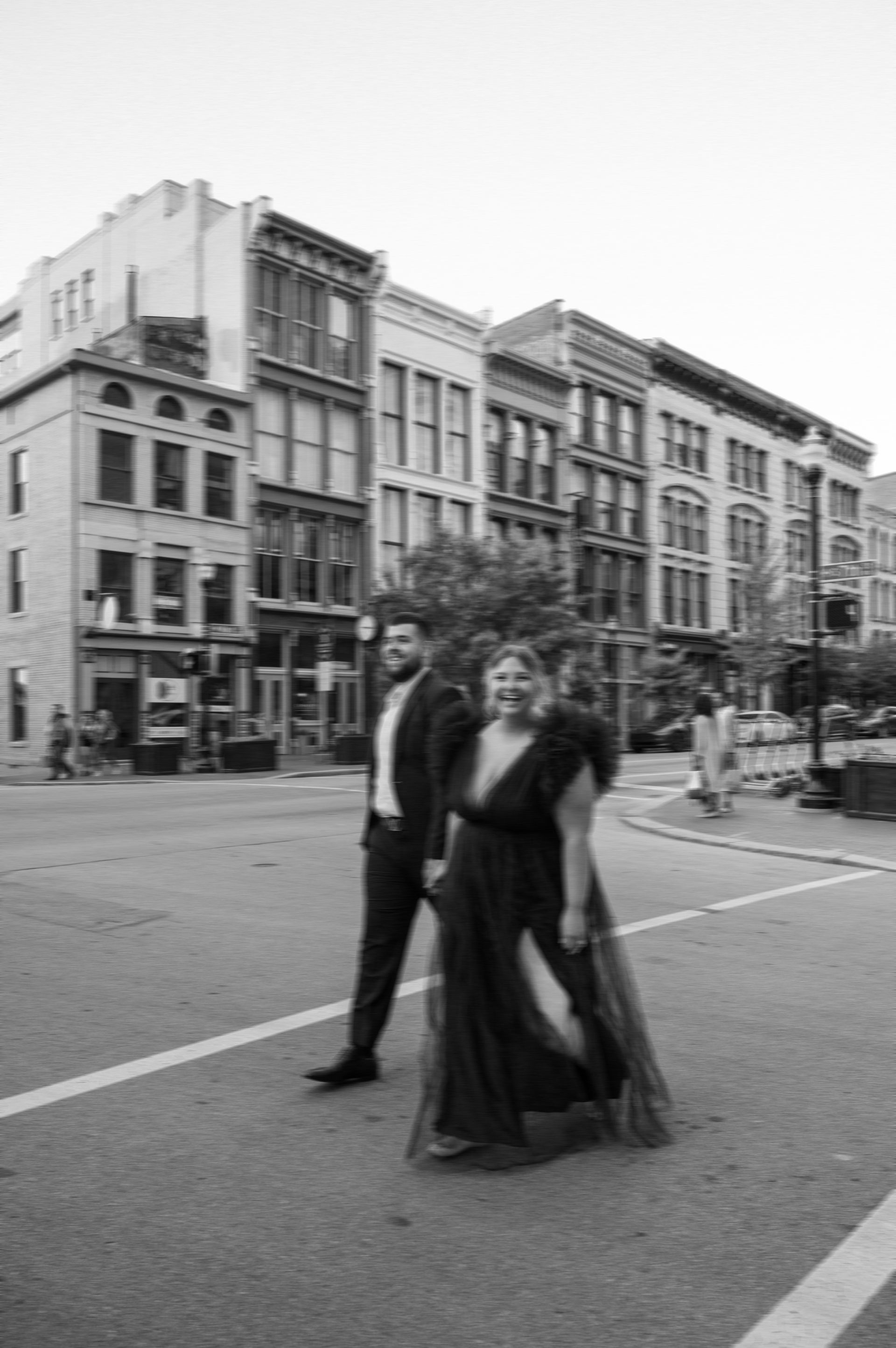 A black and white photo of a man and woman crossing a street.
