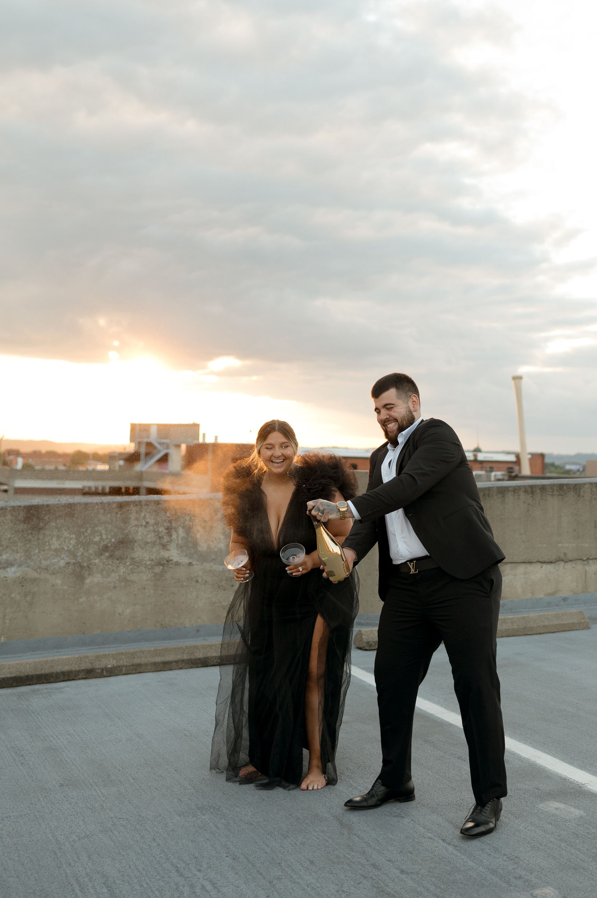 A man in a suit is holding a bottle of champagne next to a woman in a black dress.