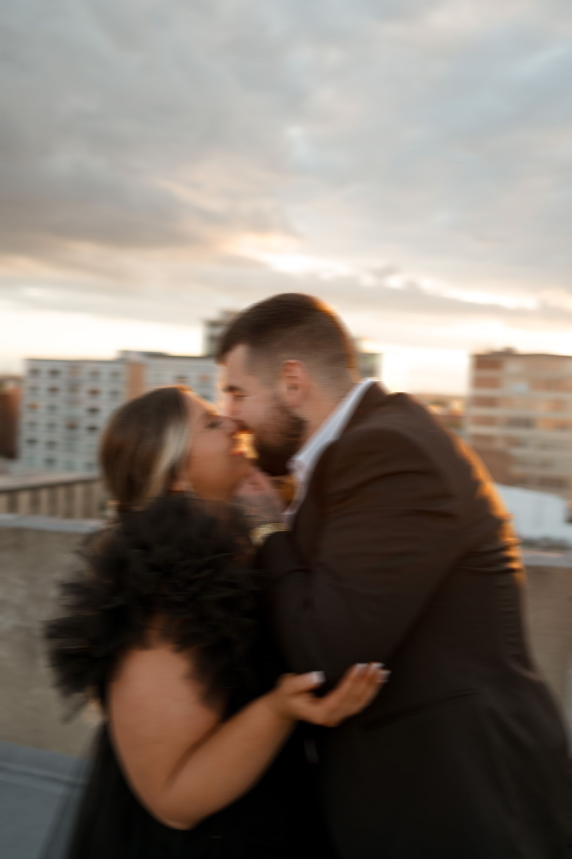A man and a woman are kissing on a rooftop at sunset.
