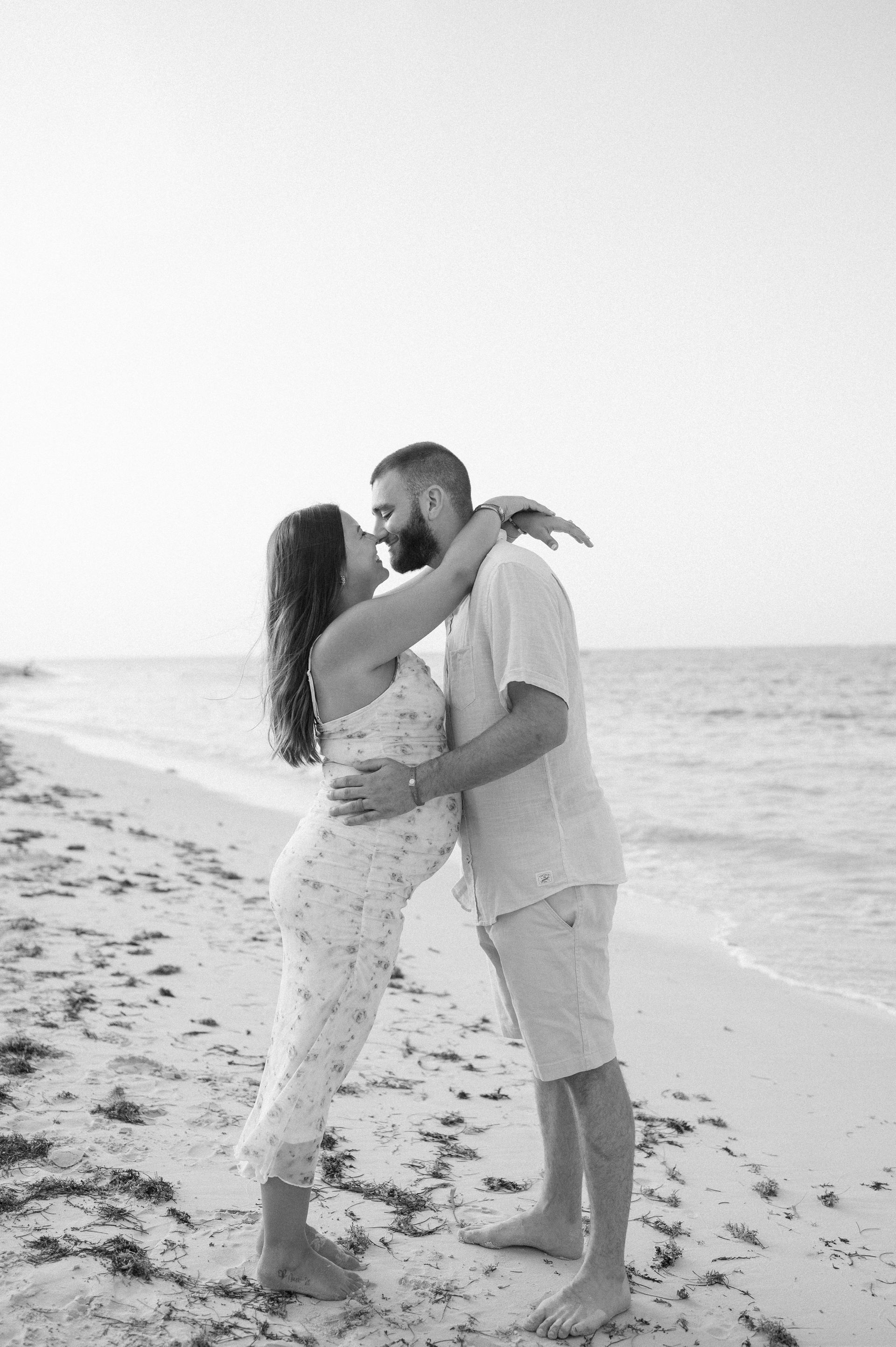 A man and a pregnant woman are kissing on the beach.