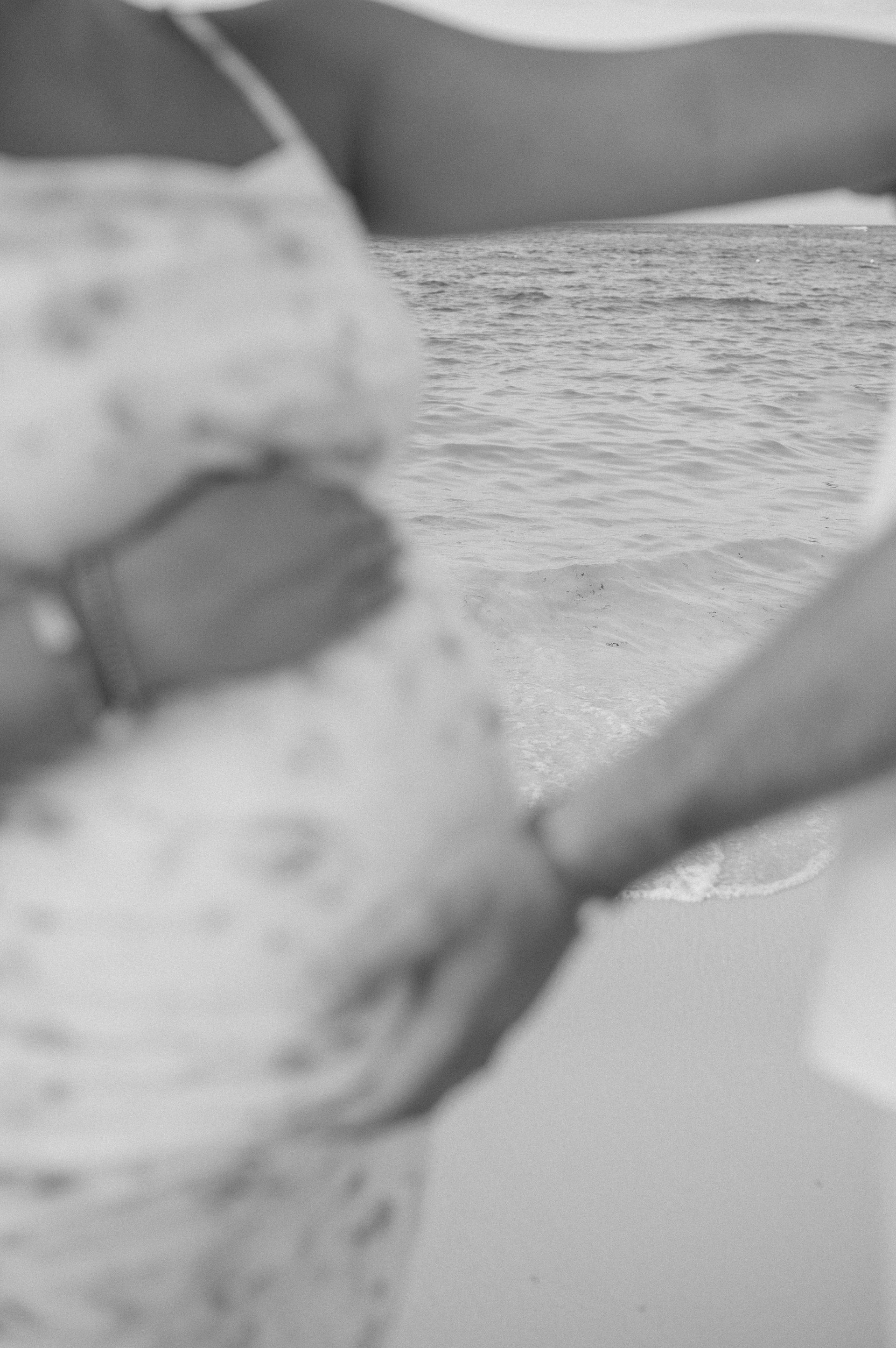 A black and white photo of a pregnant woman holding hands on the beach.