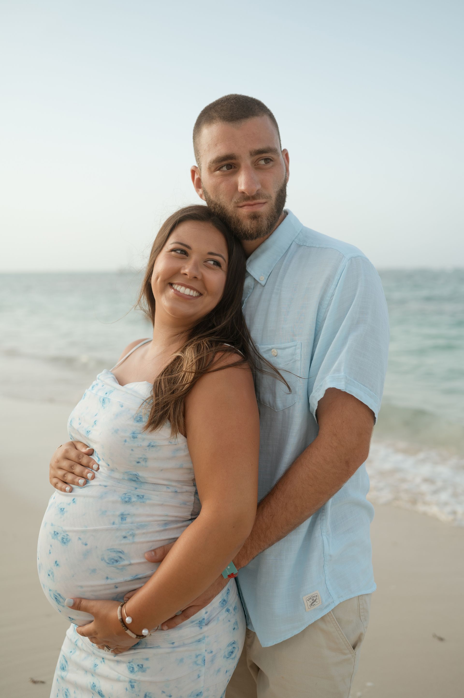 A man and a pregnant woman are posing for a picture on the beach.