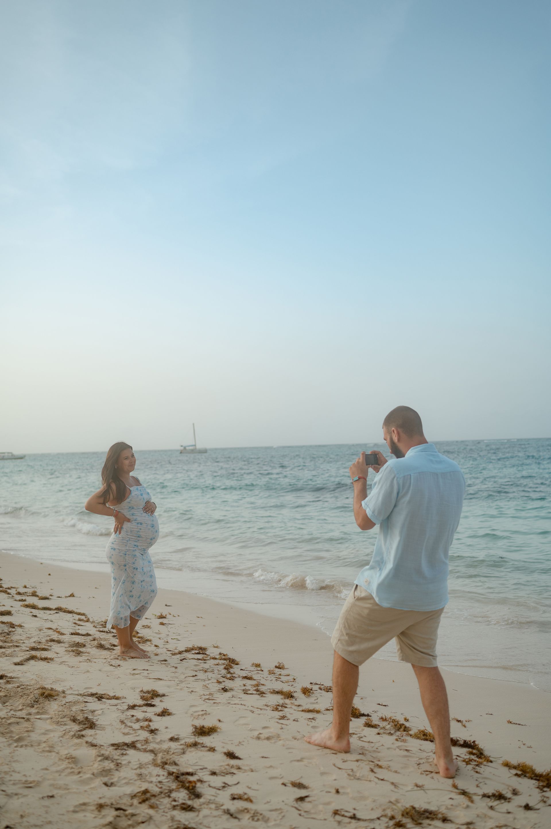 A man is taking a picture of a pregnant woman on the beach.