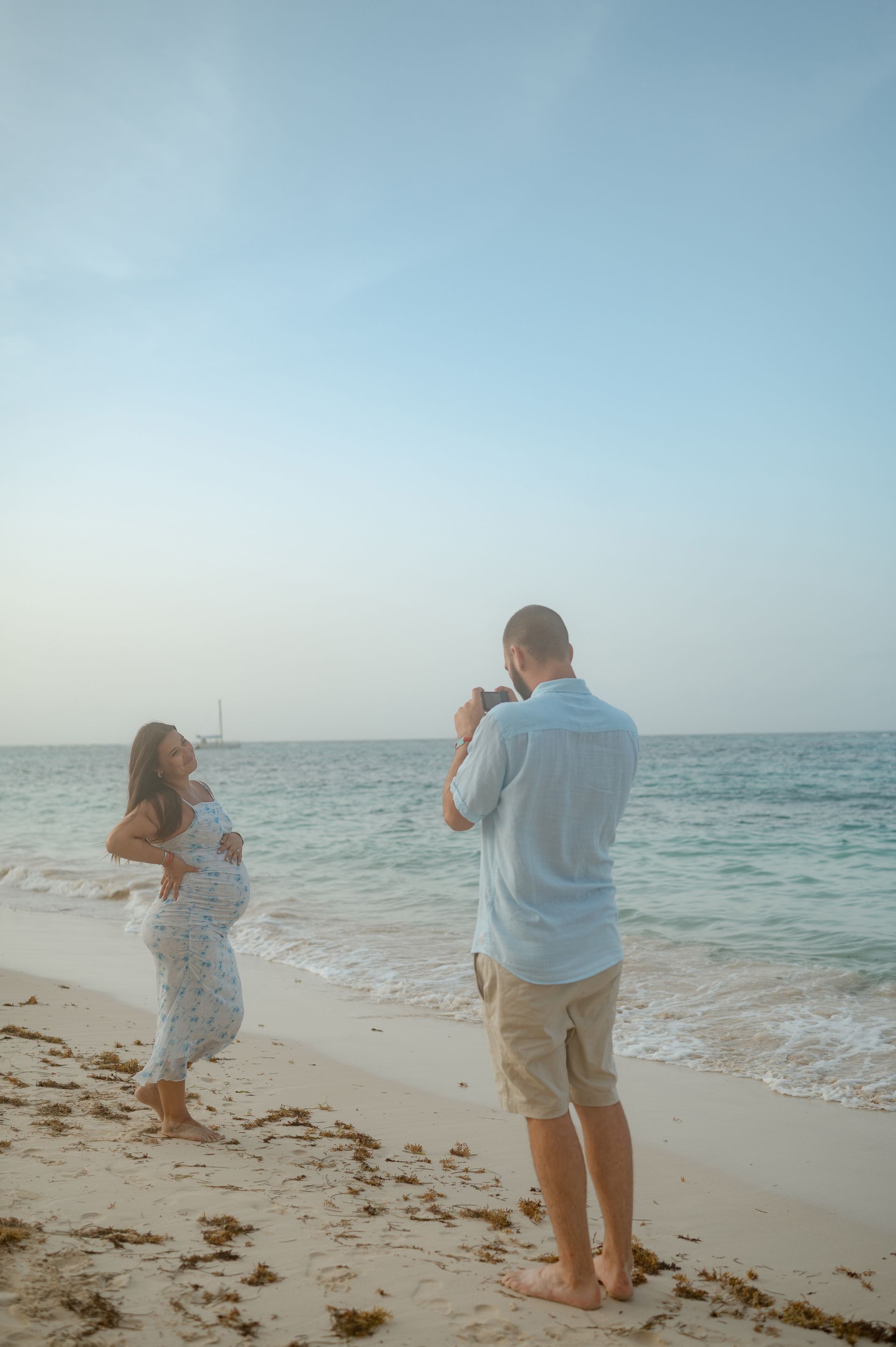 A man is taking a picture of a pregnant woman on the beach.
