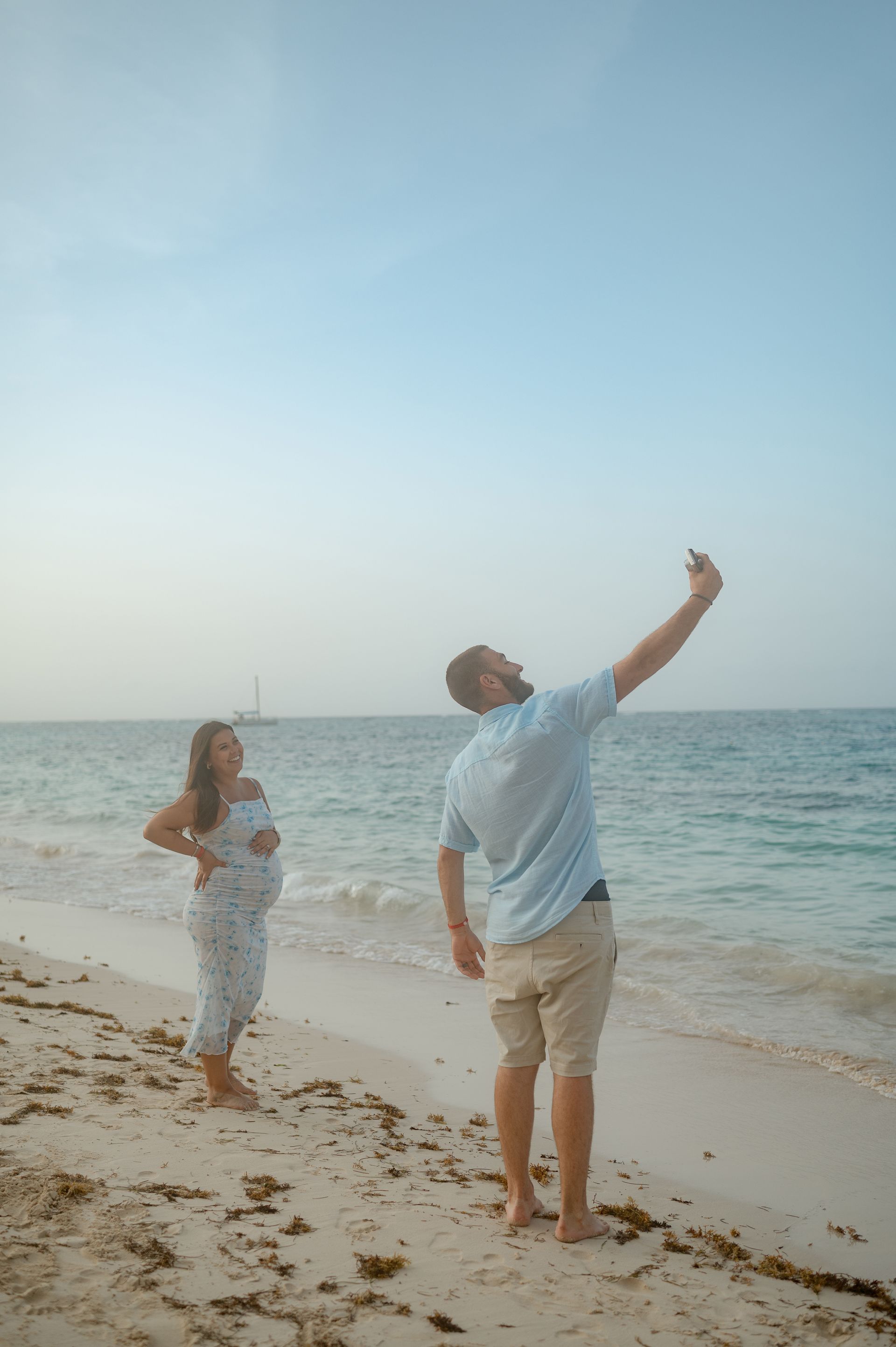 A man and a pregnant woman are taking a selfie on the beach.