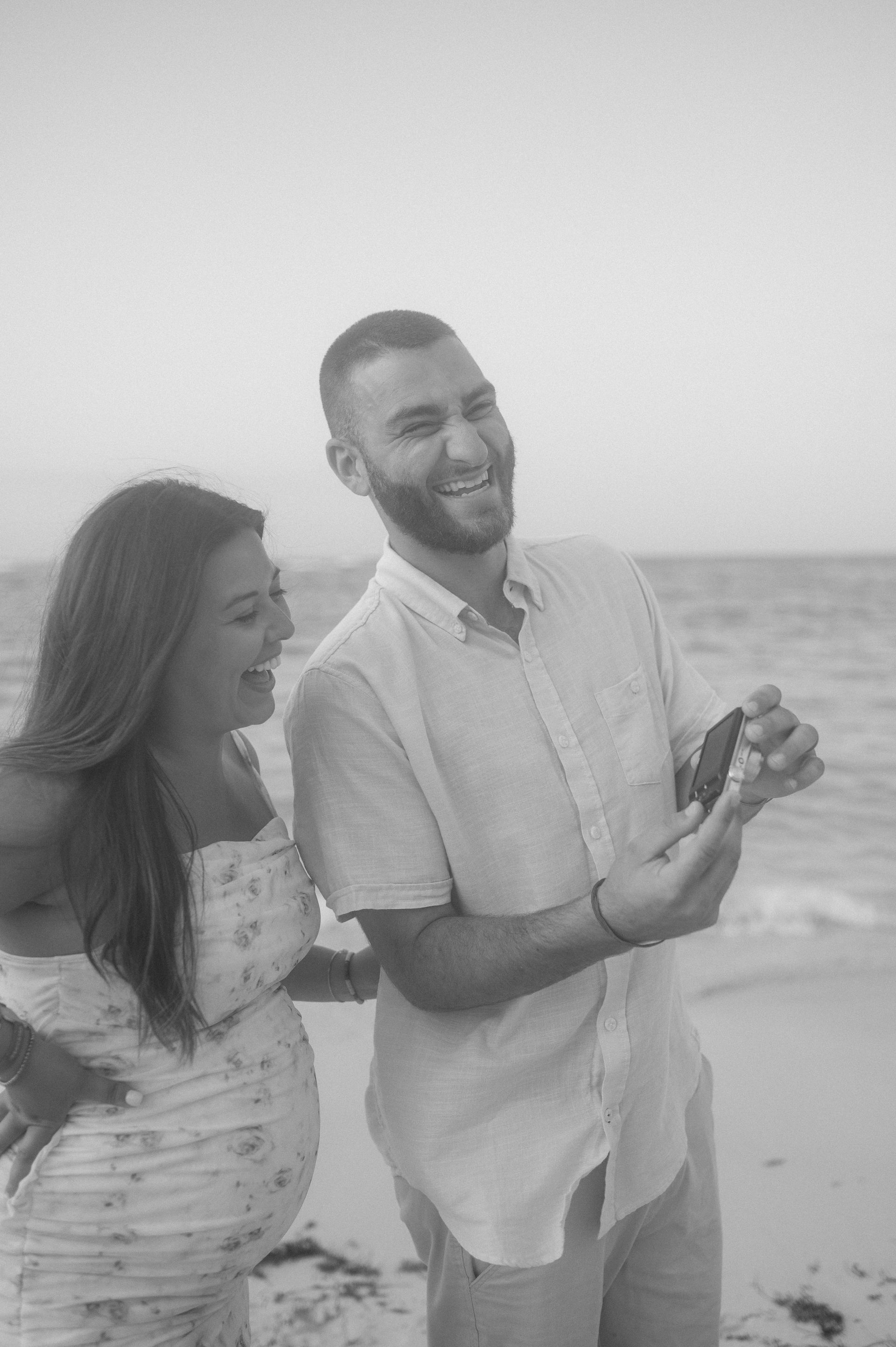 A man and a pregnant woman are standing on a beach.