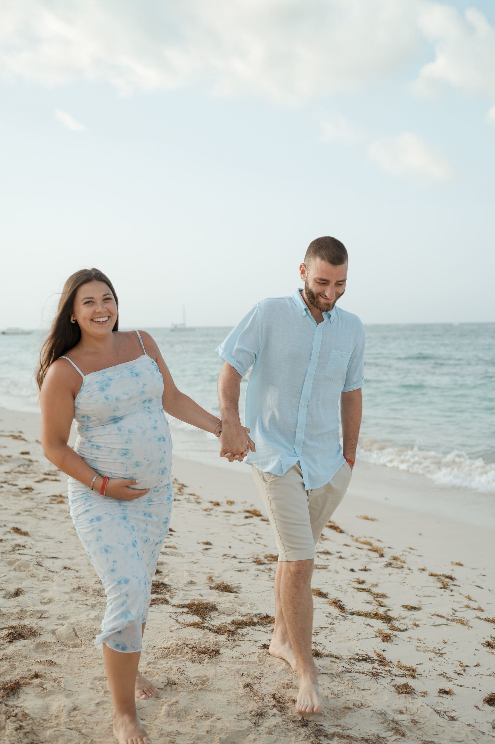 A man and a pregnant woman are walking on the beach holding hands.