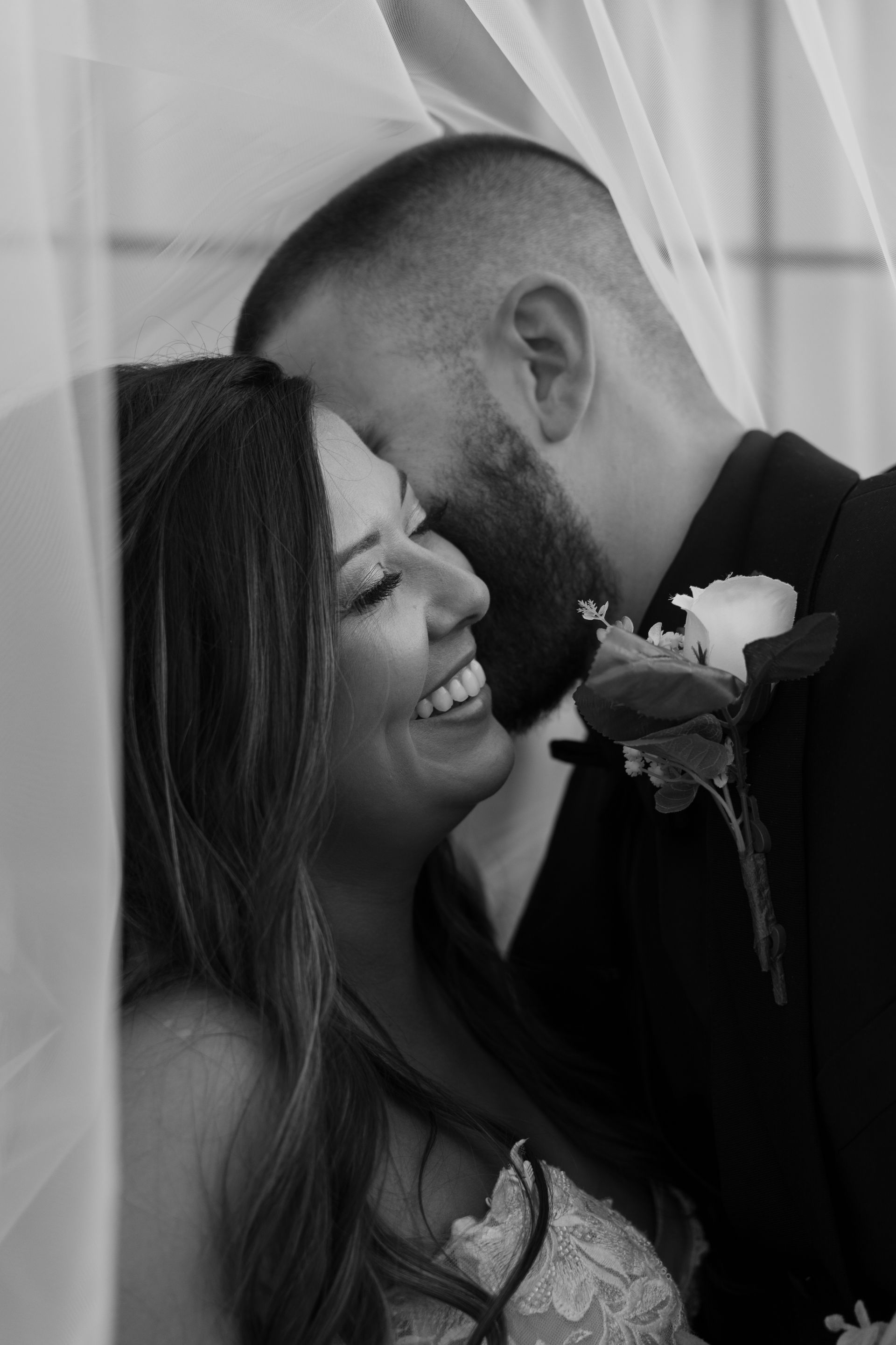 A bride and groom are kissing under a veil on their wedding day.
