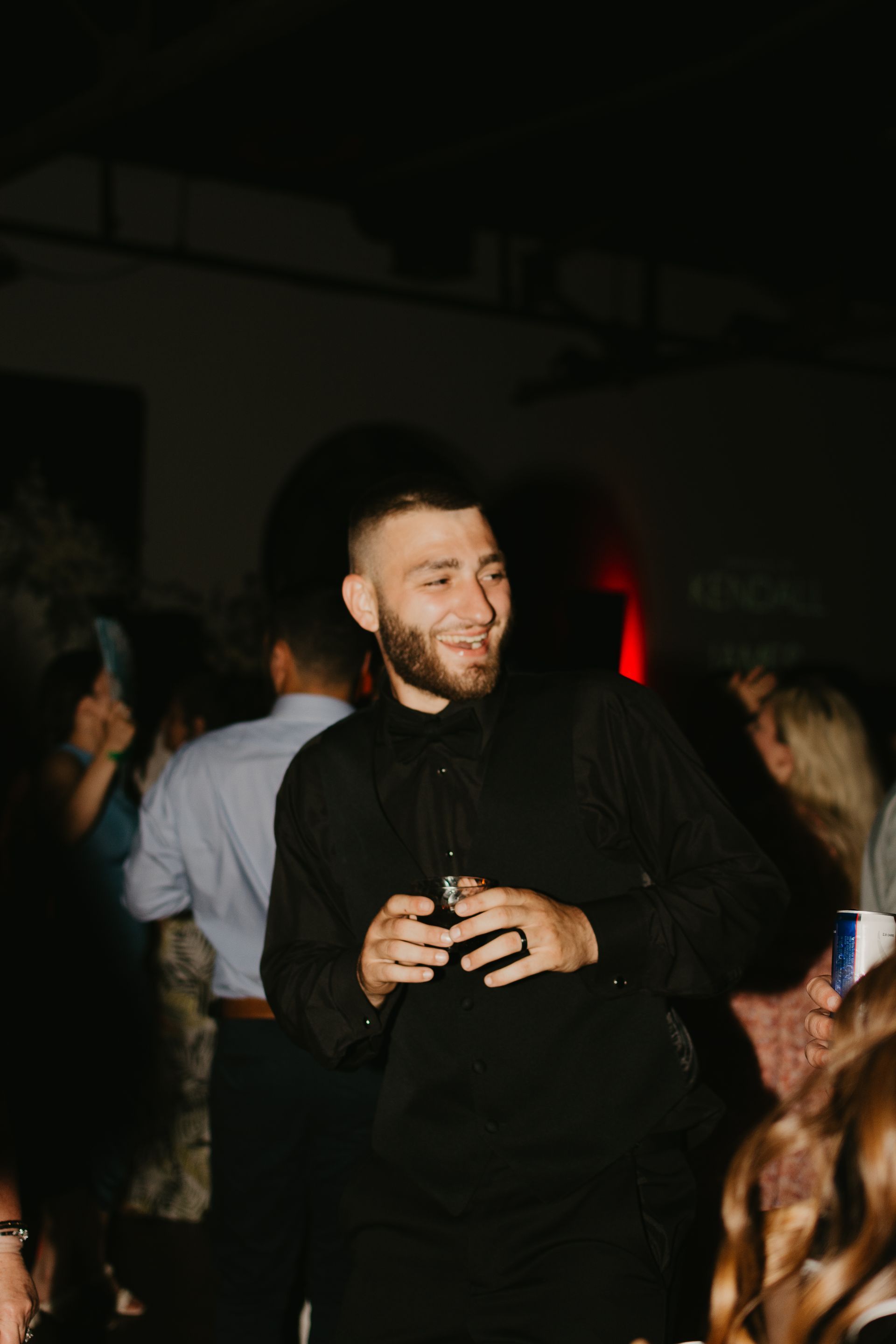 A man in a black shirt is holding a glass of beer in a dark room.