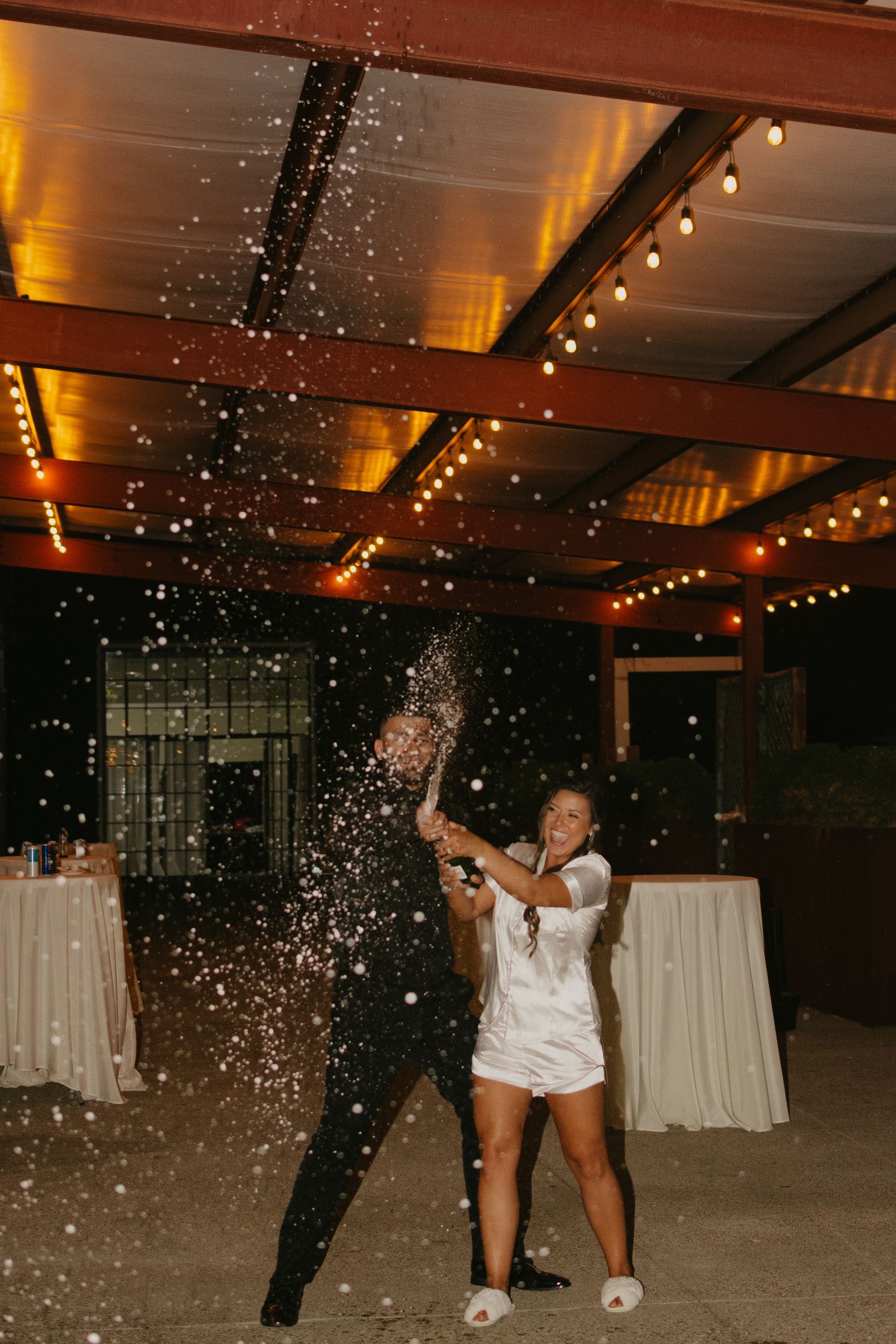 A man and a woman are standing in a room holding a bottle of champagne.