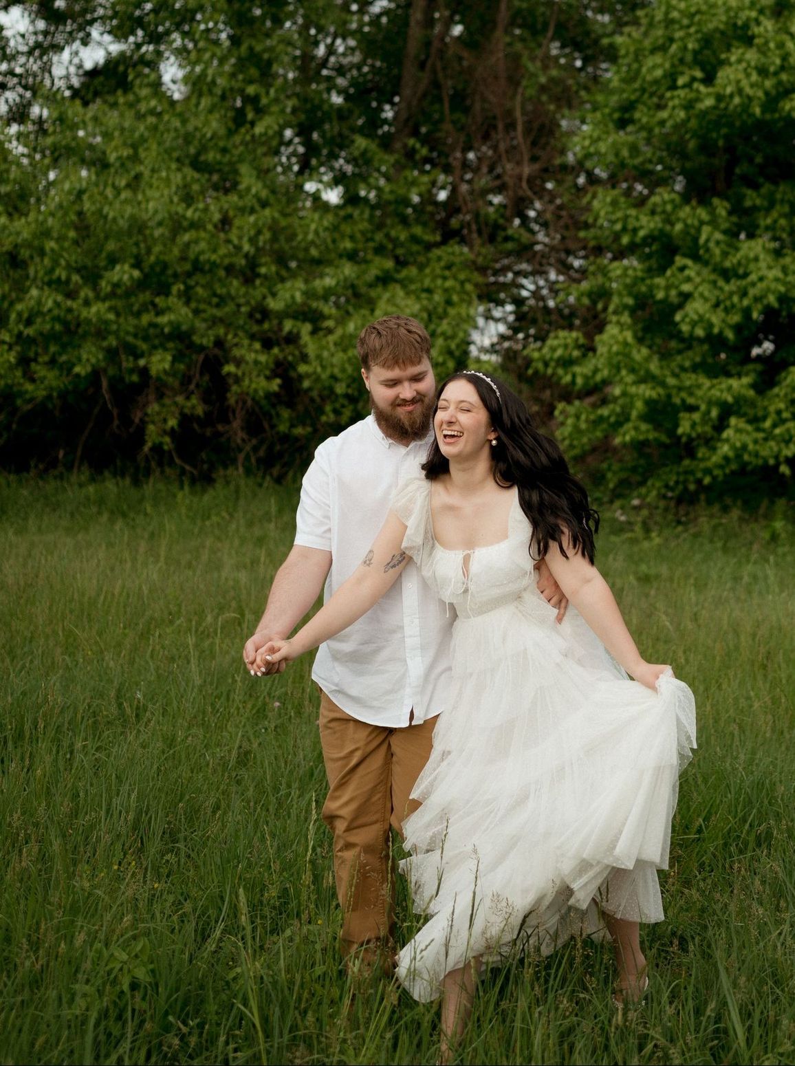 A bride and groom are running through a grassy field holding hands.