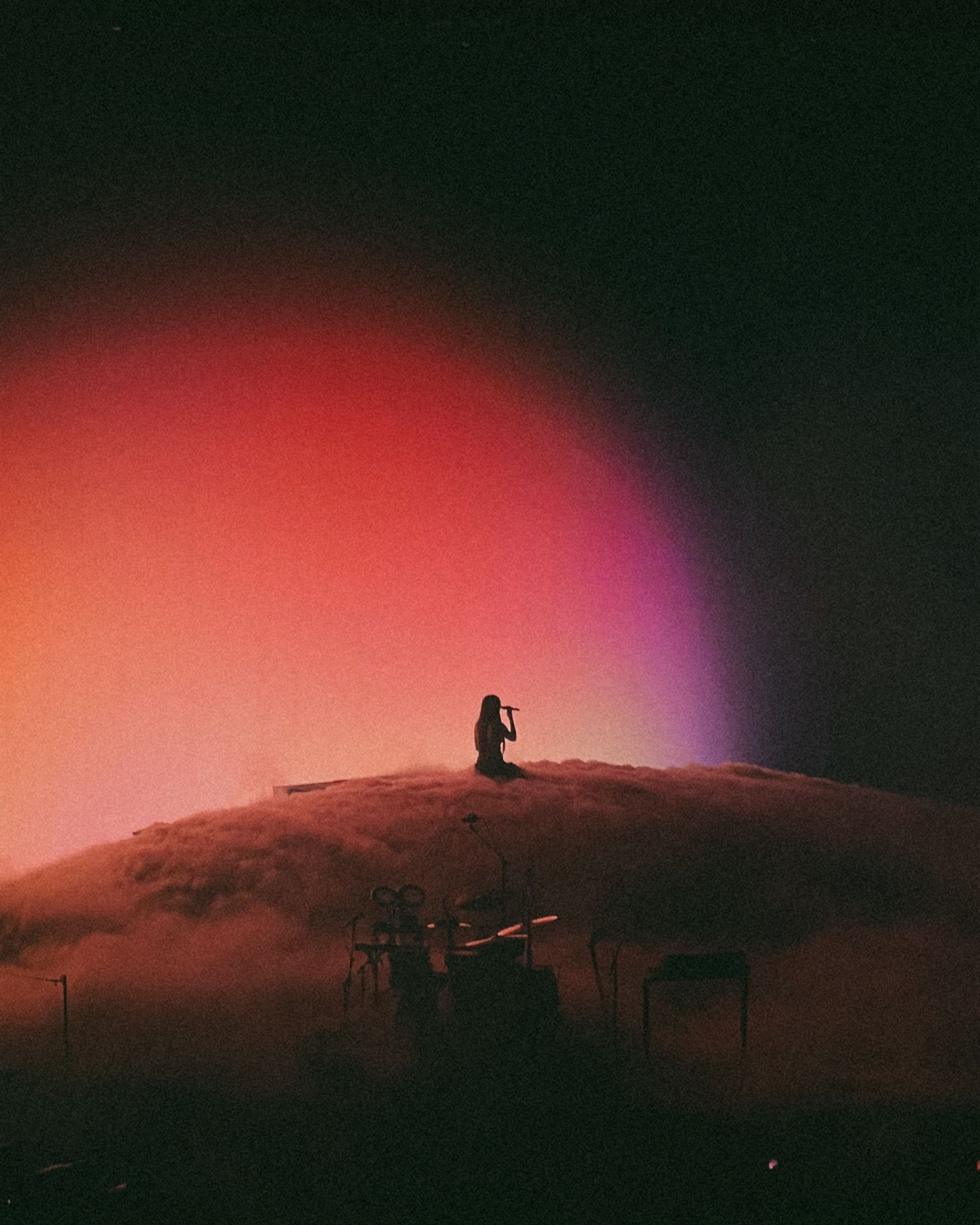 A person is standing on top of a hill with a rainbow in the background.