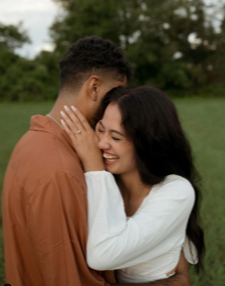 A man and a woman are hugging each other in a field . the woman is wearing a ring on her finger.