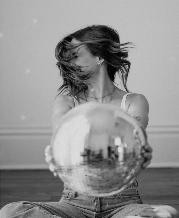 A woman is sitting on the floor holding a disco ball.