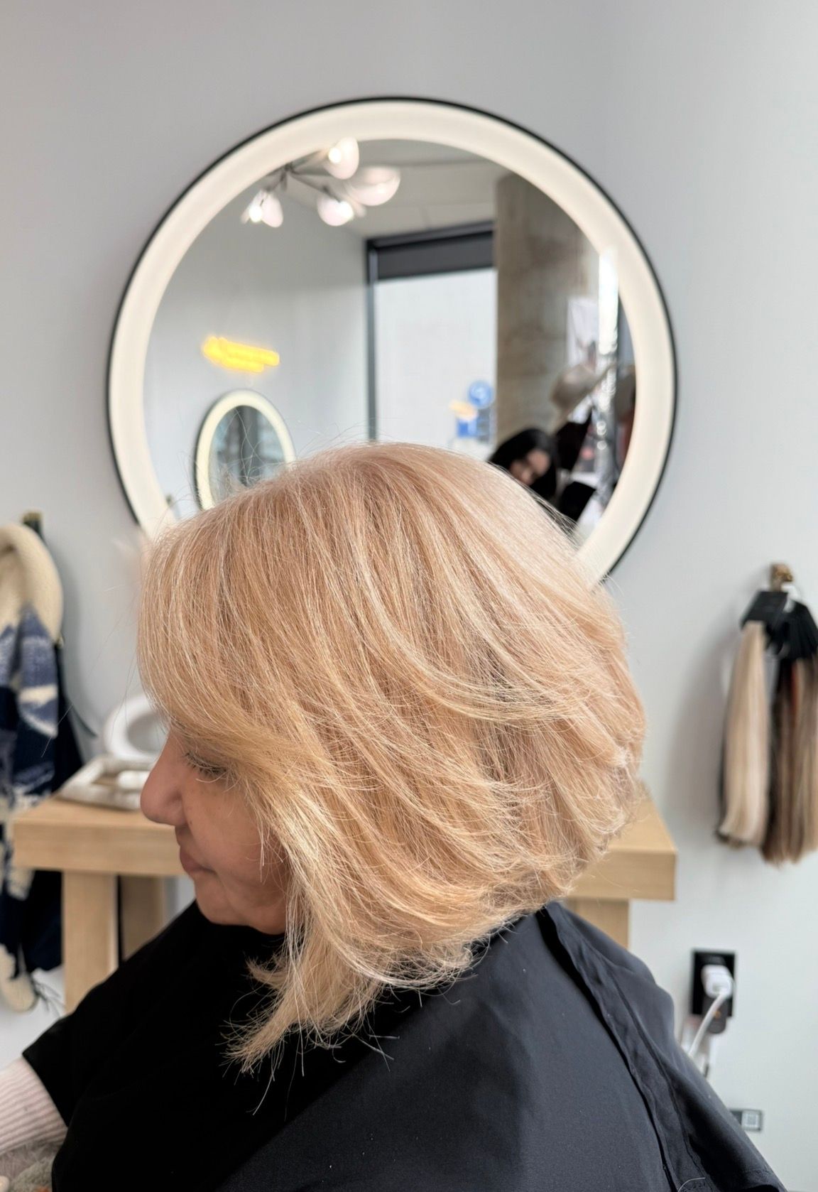Woman with layered, light-colored hair, in a salon, near a mirror.