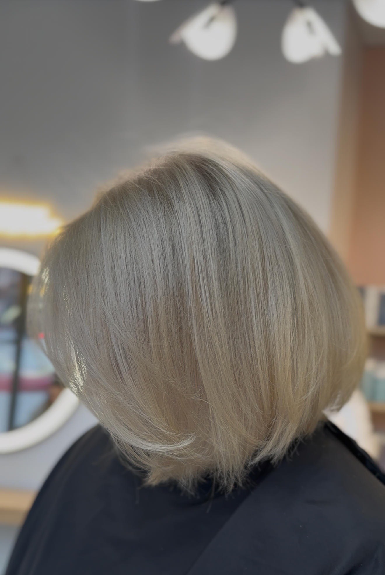 Back view of a person with short, layered, light blonde hair in a salon setting.