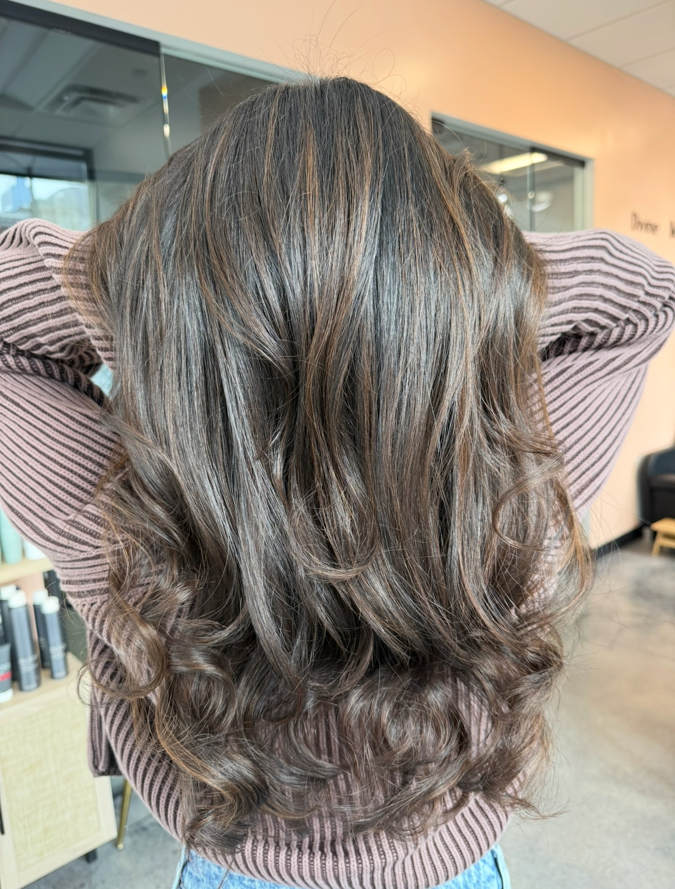 Person with layered dark brown hair, hands behind head, in a salon setting.