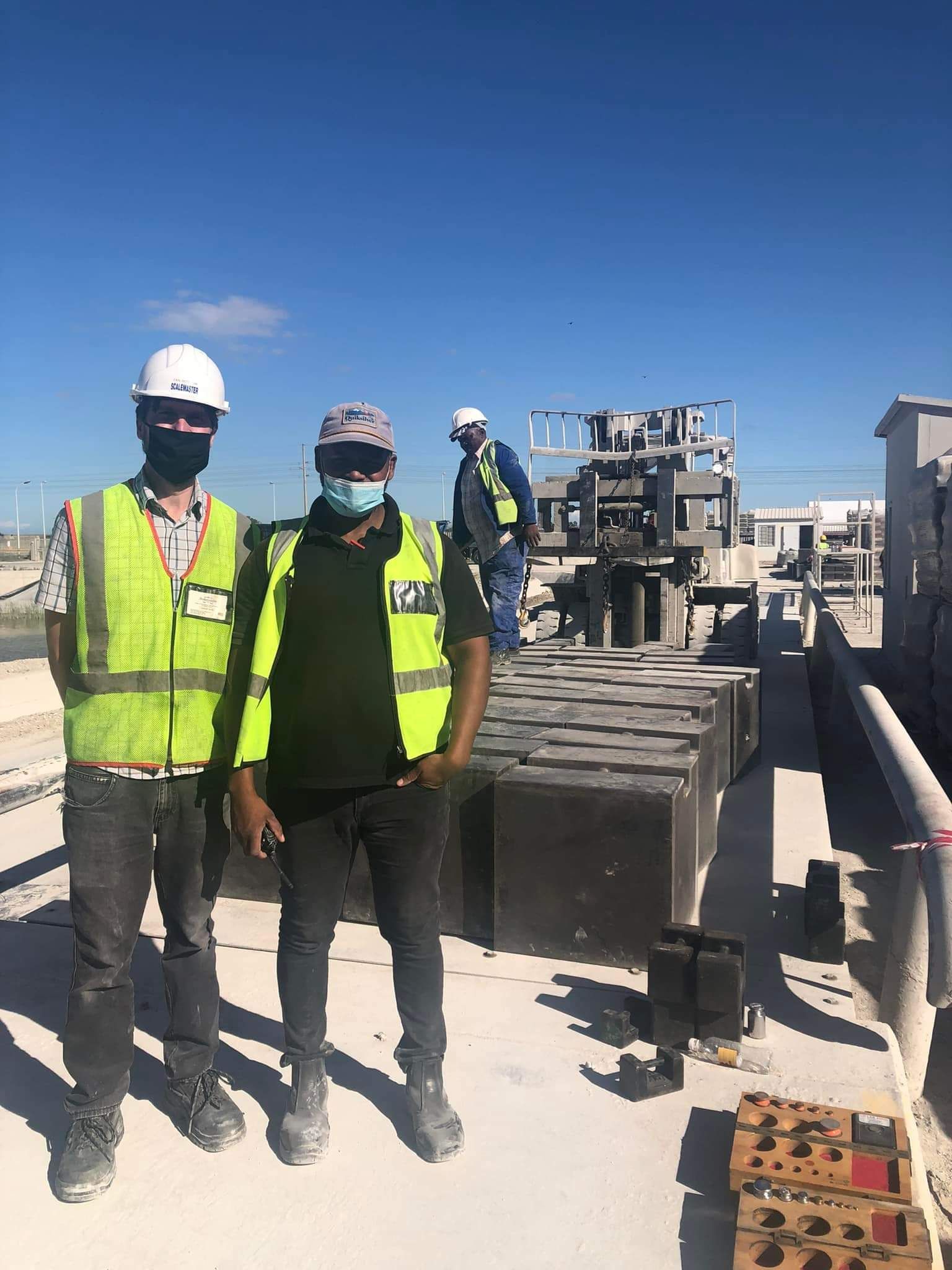 Two construction workers wearing masks and hard hats are standing next to each other on a construction site.