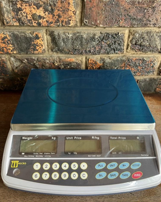 A digital scale is sitting on a wooden table in front of a brick wall.