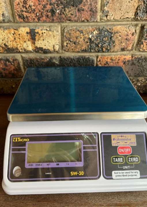 A digital scale is sitting on a wooden table in front of a brick wall.