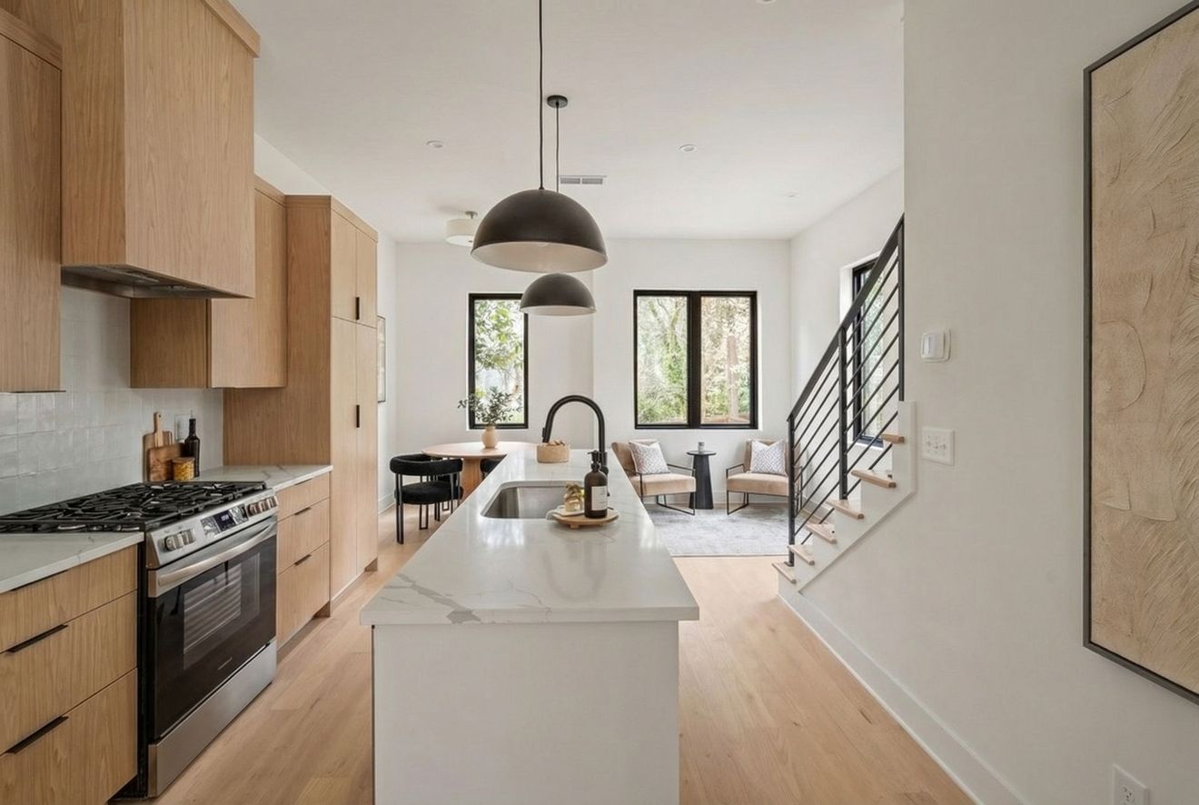 Modern kitchen with light wood cabinets, a white marble island, black appliances, and a staircase leading to a dining area.