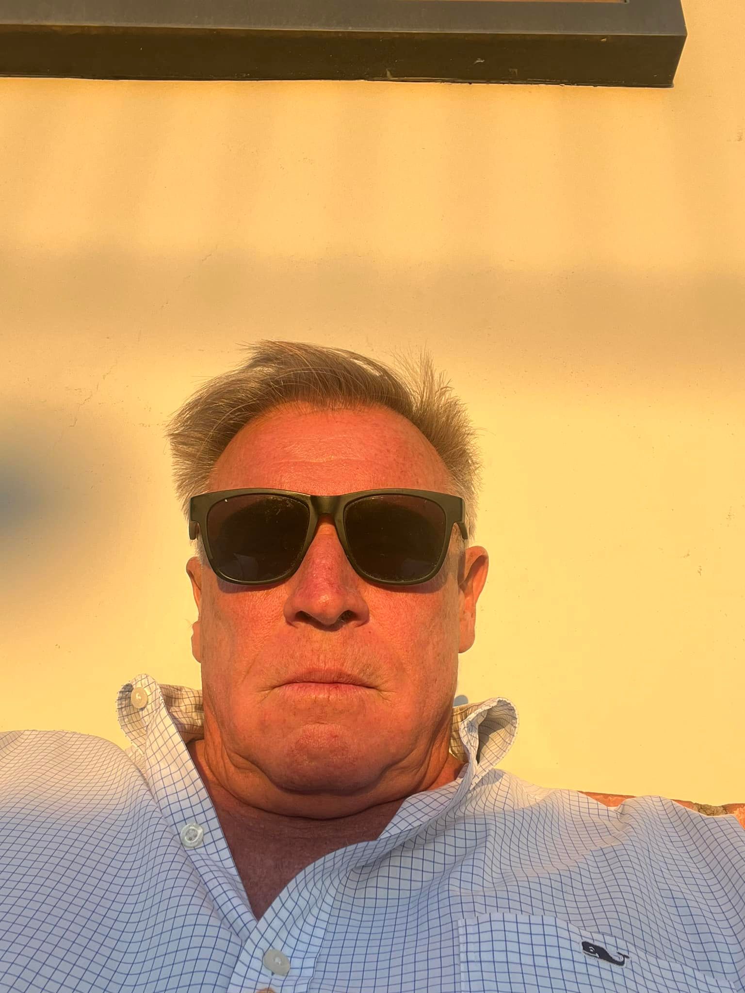A man wearing sunglasses and a white shirt is taking a selfie.