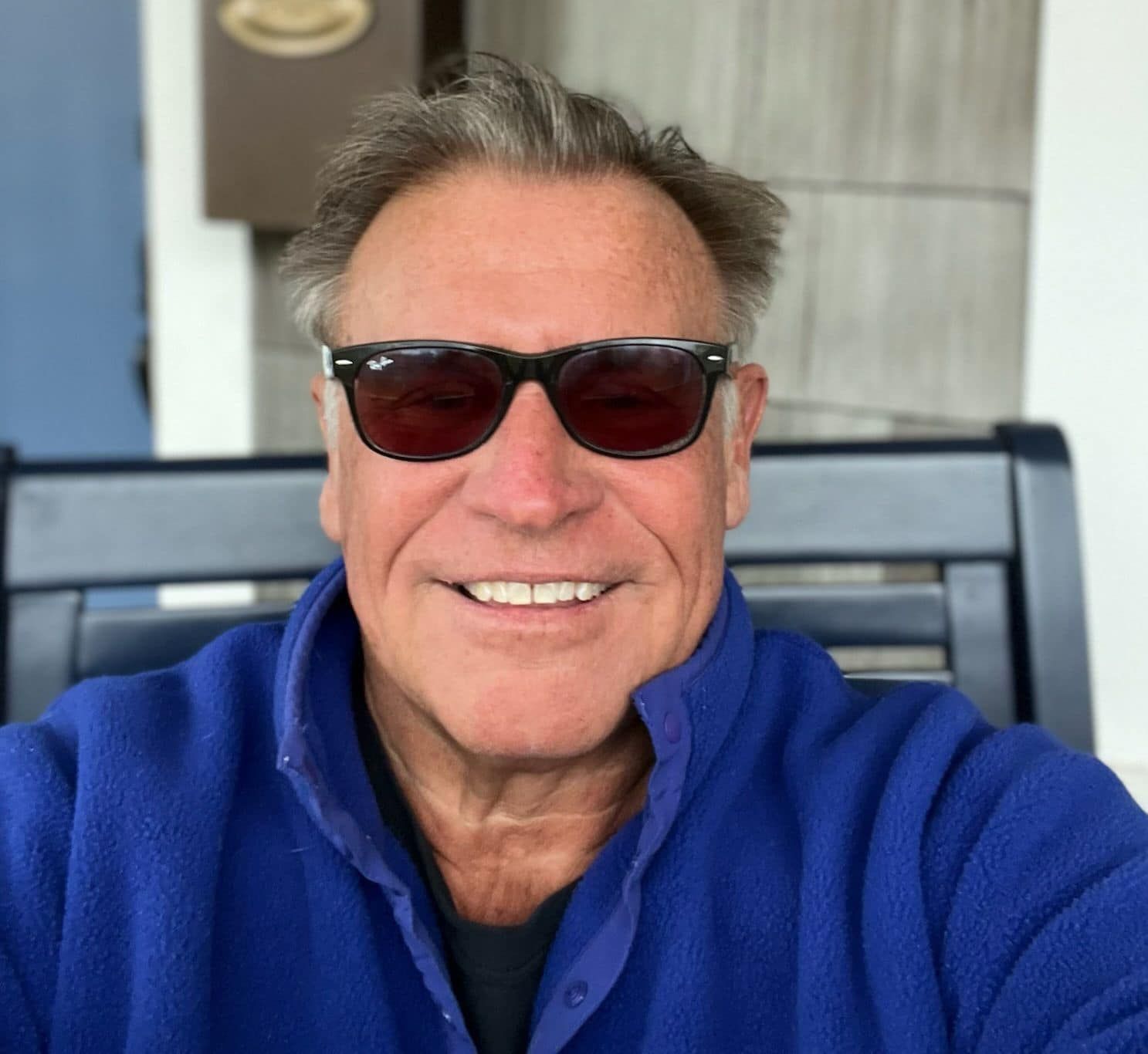 A man wearing sunglasses and a blue sweater is smiling for the camera.