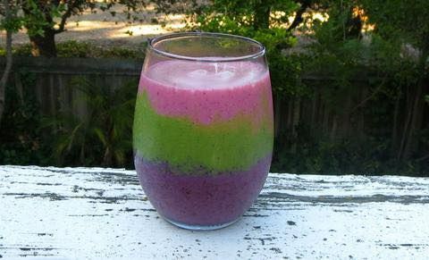 A rainbow colored smoothie in a wine glass on a table.