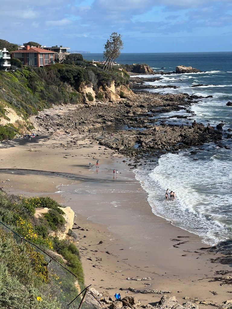 A beach with a house on the cliff and a lighthouse in the distance.
