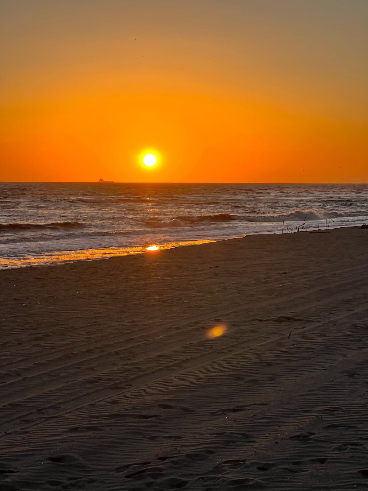 The sun is setting over the ocean on a beach.