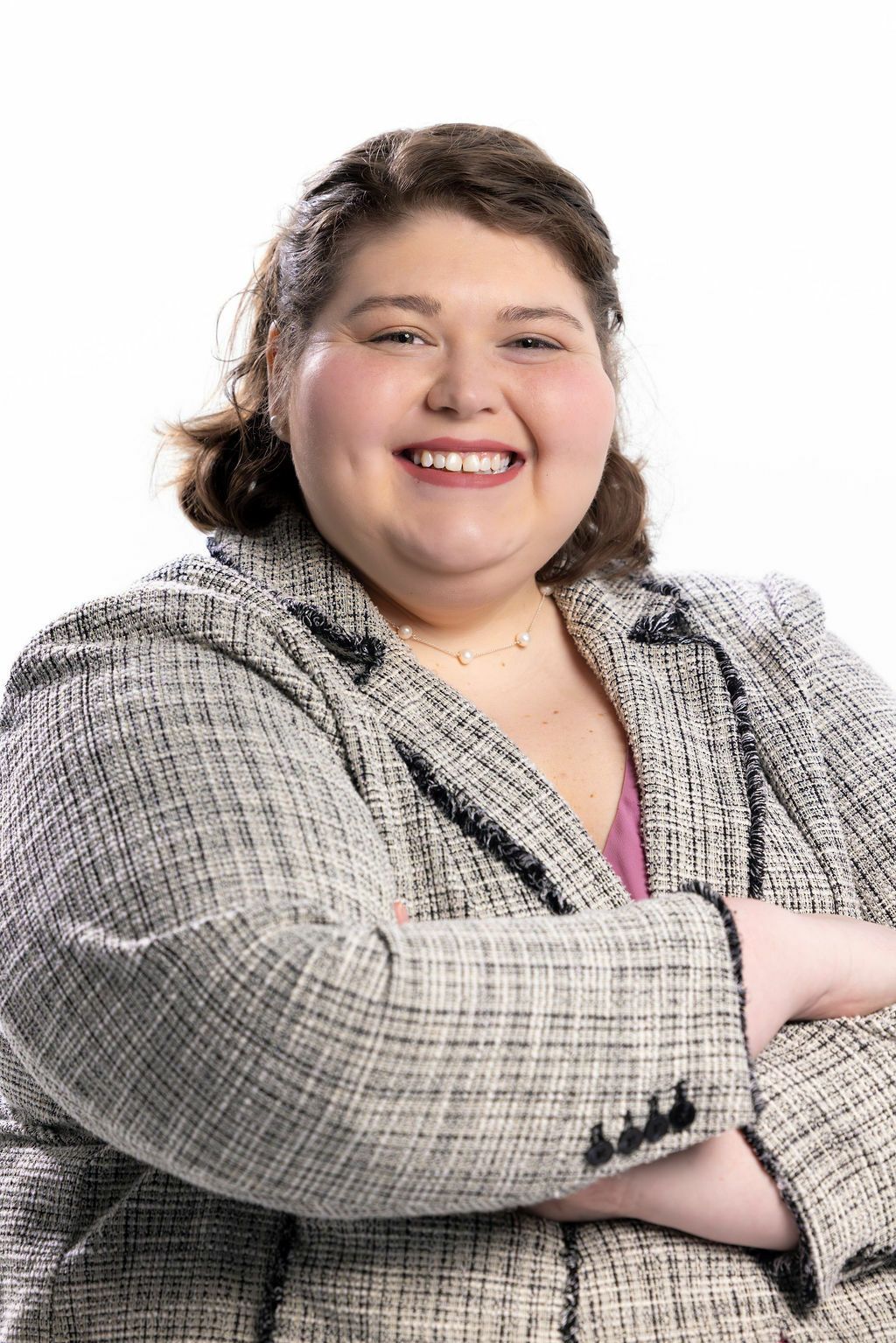 A woman in a suit is smiling with her arms crossed.