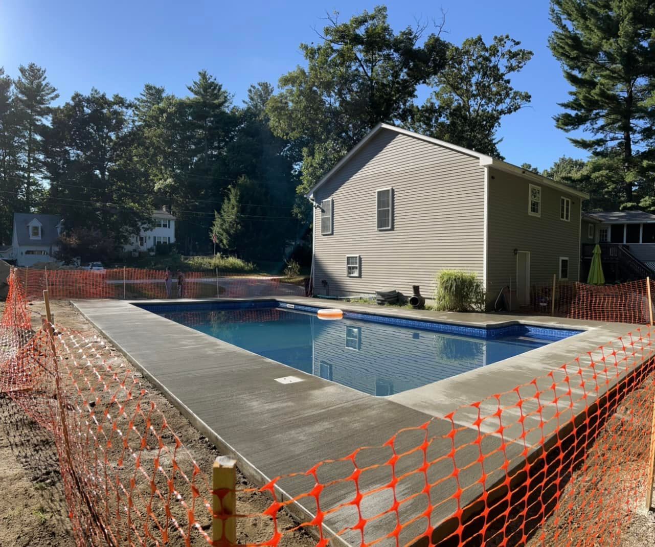A large swimming pool is surrounded by a fence and a house.