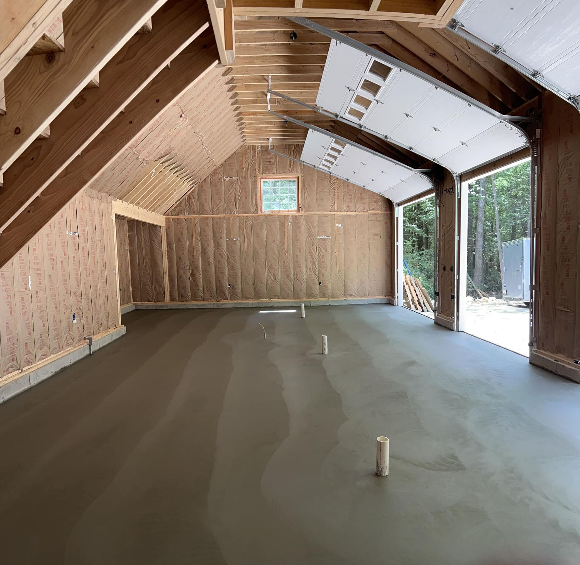 A garage under construction with a concrete floor and a garage door open.