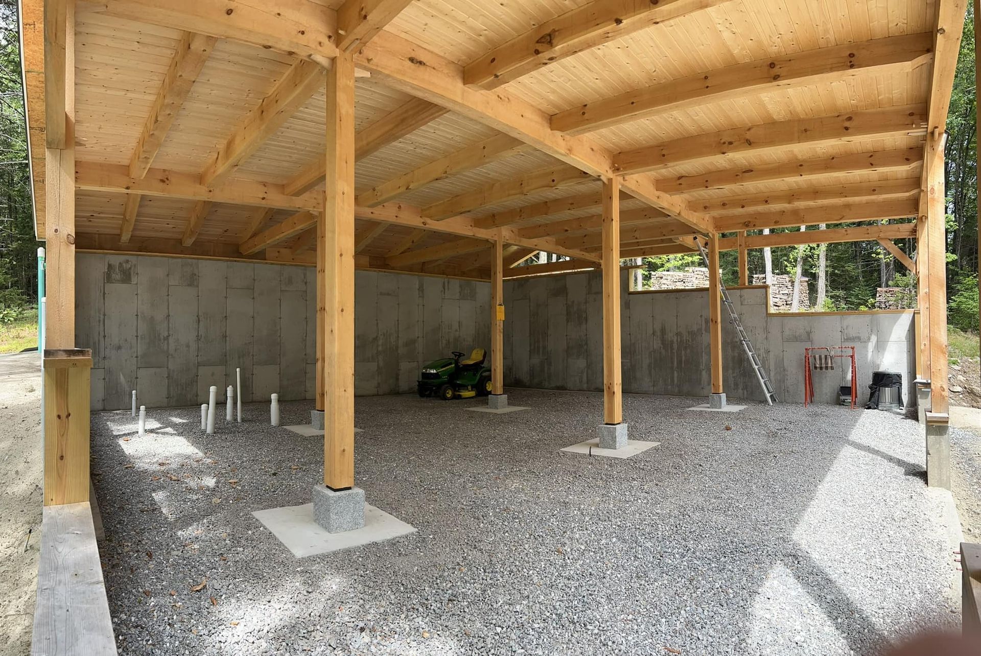 A tractor is parked under a wooden structure in a gravel area.