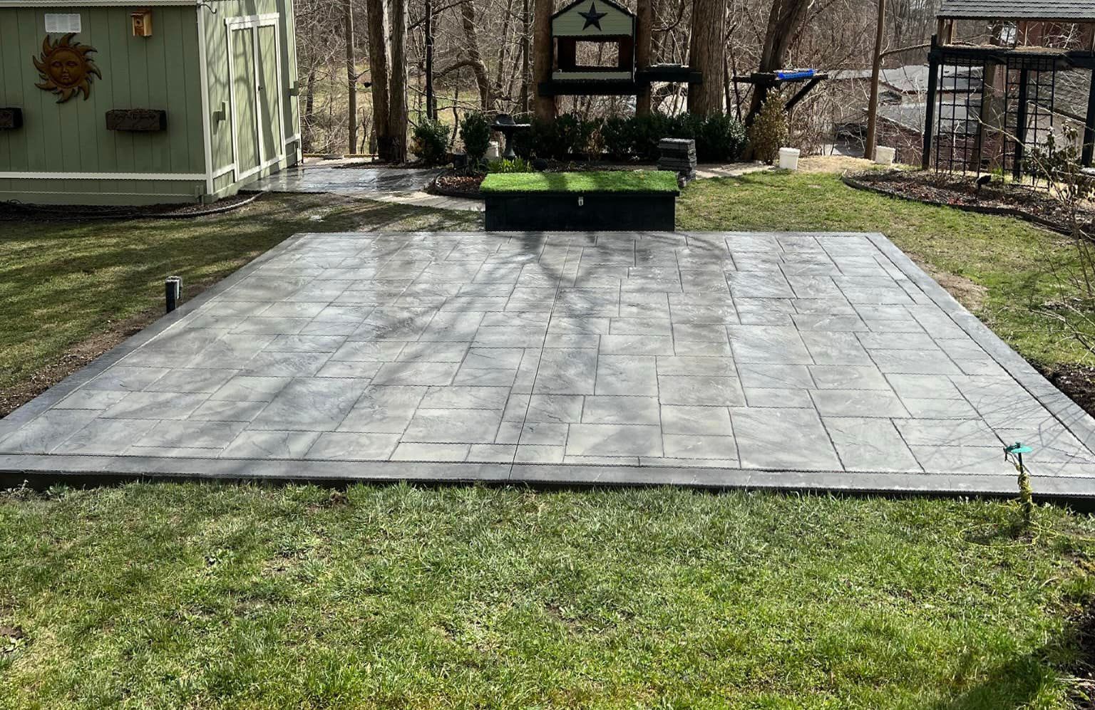 A large concrete patio in the middle of a lush green yard.