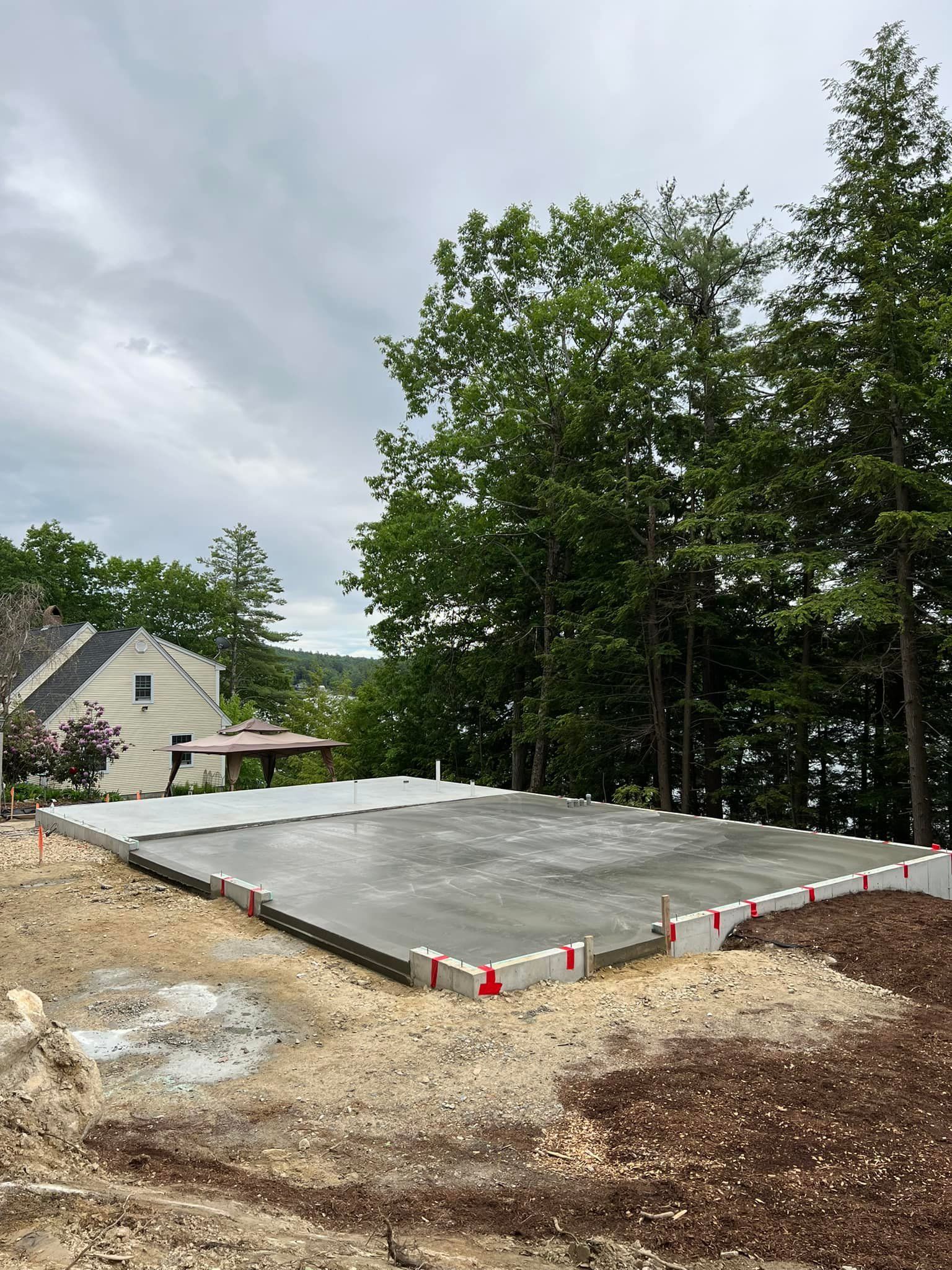 A large concrete slab is sitting in the middle of a dirt field in front of a house.